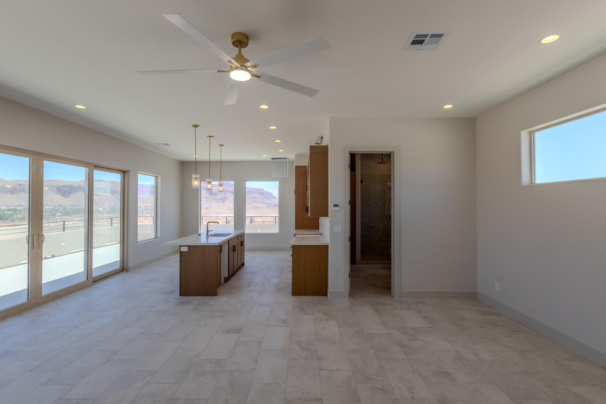 Spacious open-concept room featuring light-toned tile flooring, a contemporary ceiling fan, recessed lighting, and a kitchen island with pendant lighting