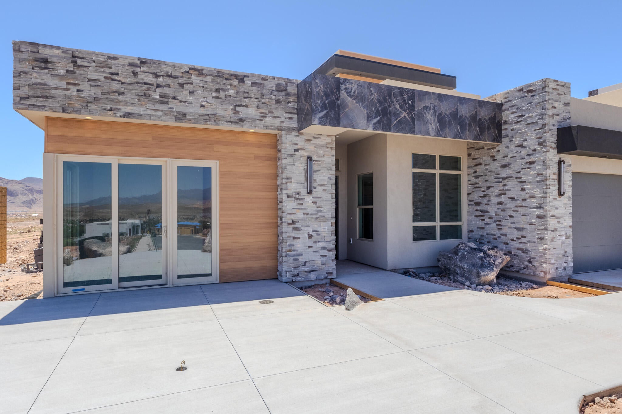 Modern exterior featuring stacked stone accents, wood-finish siding, a smooth stucco finish, a contemporary front entry, and a multi-panel sliding glass door