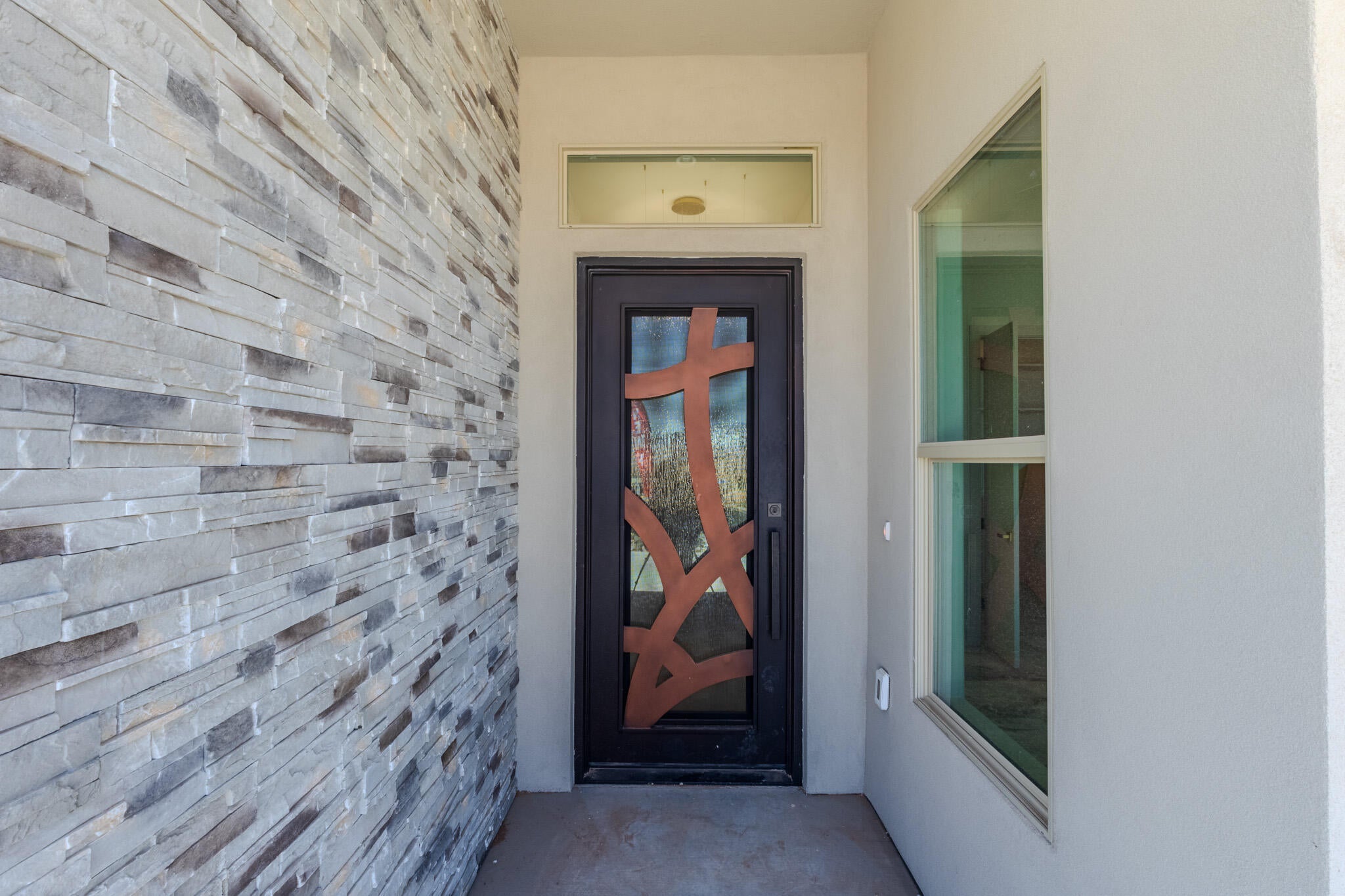 Contemporary entry with a decorative metal-paneled front door, stacked stone accent wall, and stucco exterior