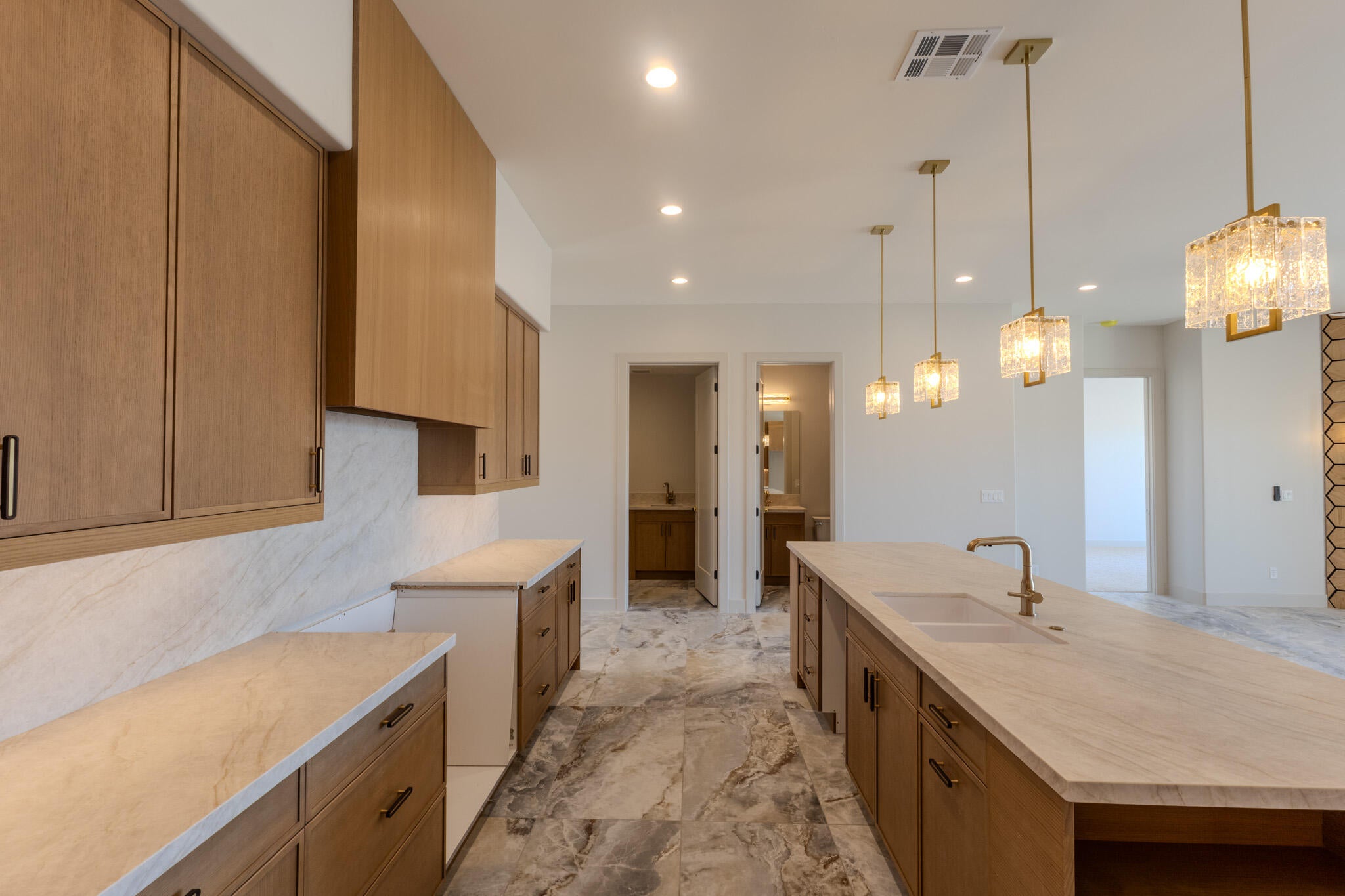 Kitchen featuring a large central island with an undermount sink and brass faucet, light wood-finish cabinetry, stone countertops, and a stone tile backsplash