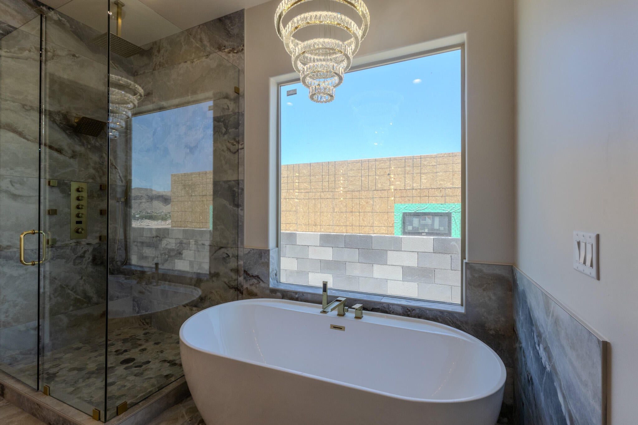 Freestanding soaking tub with gold-tone fixtures, illuminated by a contemporary chandelier
