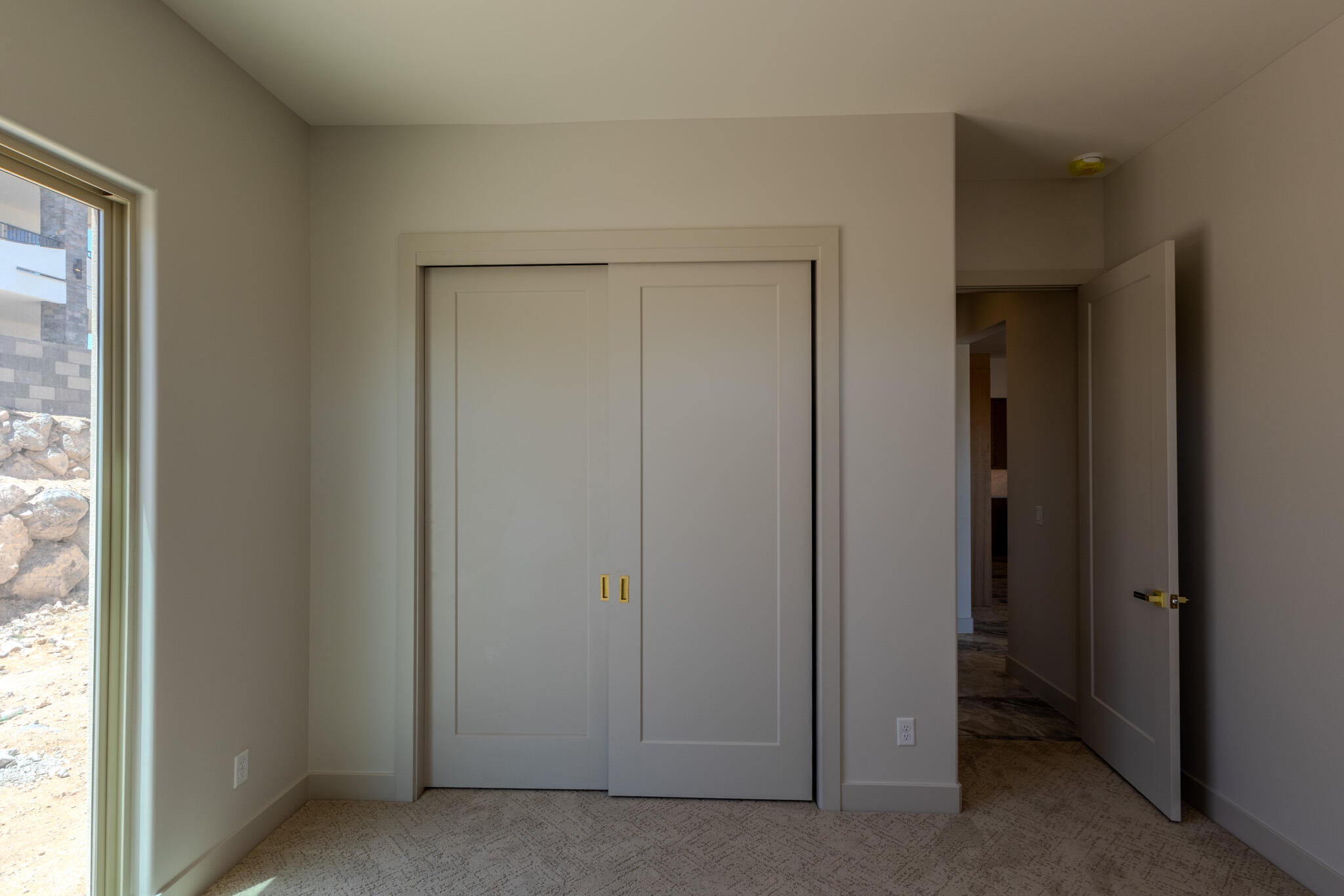 Neutral-toned room featuring a large window, sliding closet doors with gold-toned hardware, and a solid core door with a matching gold-toned handle