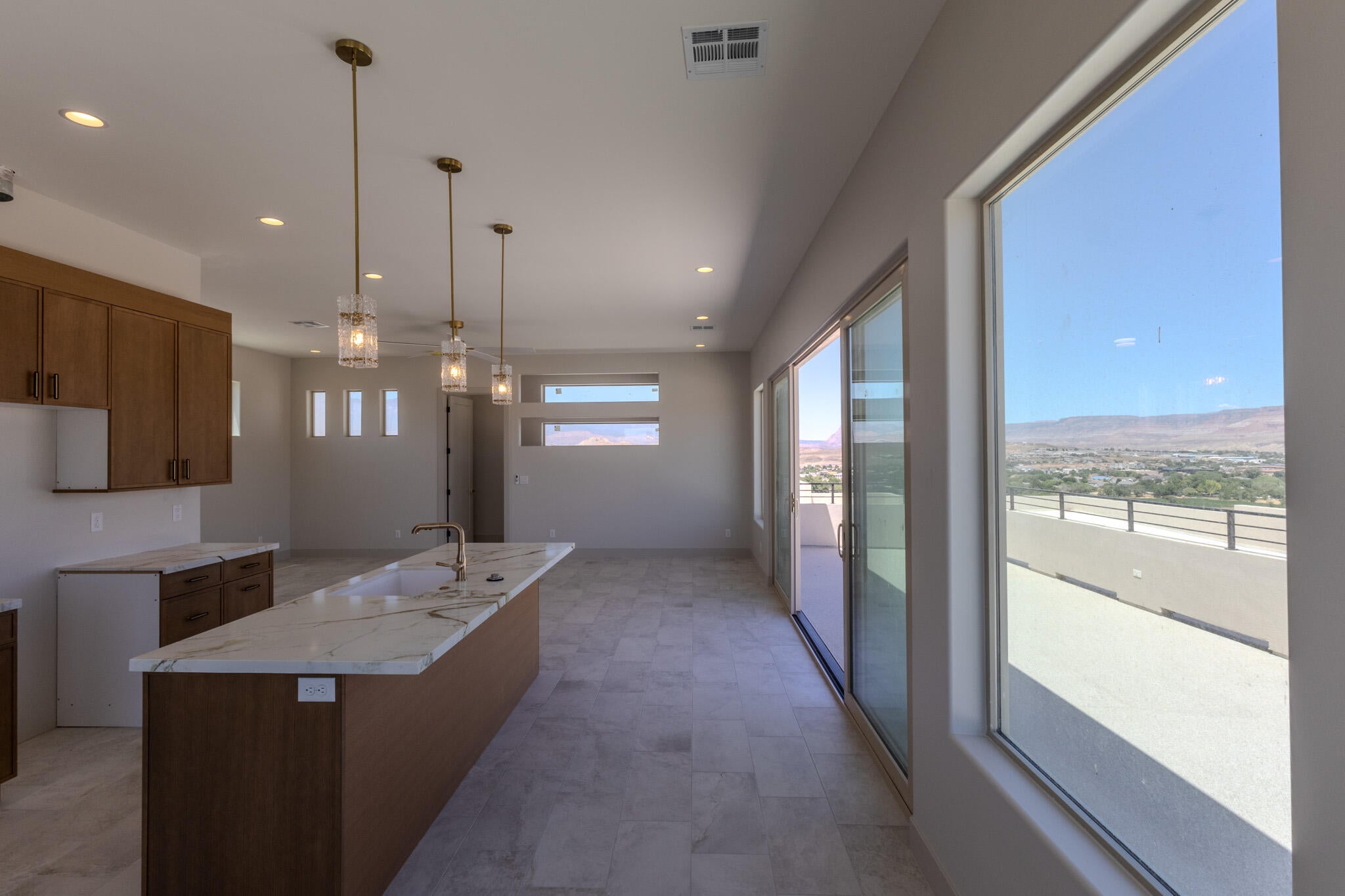 Open-concept interior featuring wood-finish cabinetry, a large kitchen island with a sink and stone countertop, recessed lighting, and multiple pendant lights
