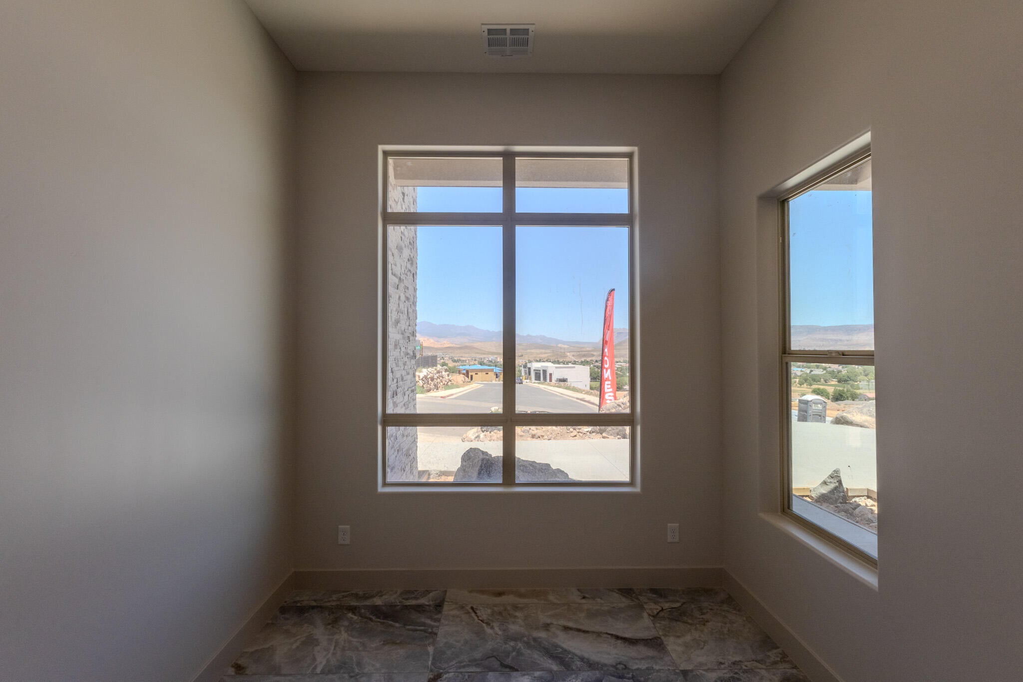 Spacious room featuring multiple windows, neutral wall tones, and large format stone-finish floor tiles