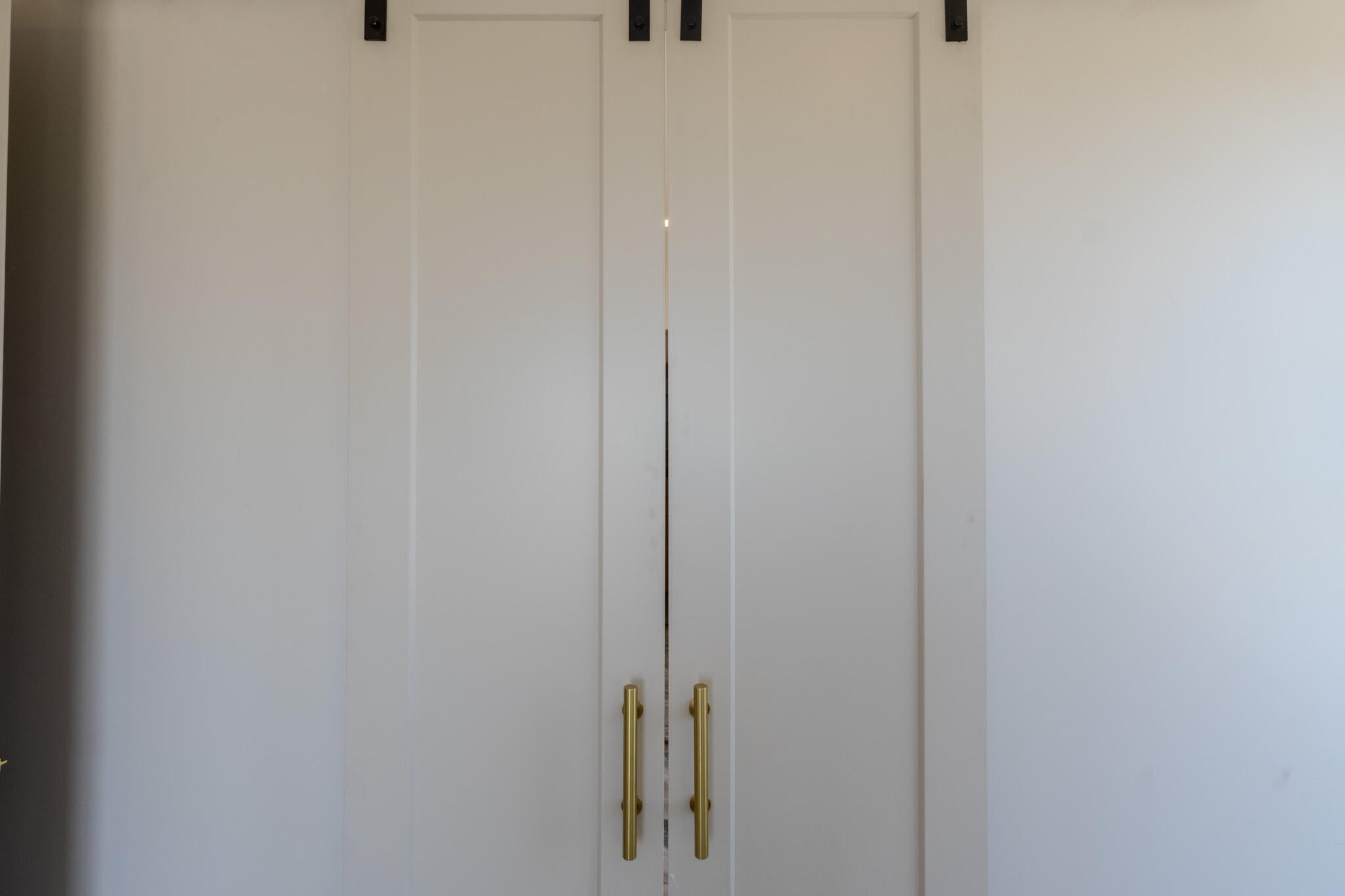White barn doors featuring black overhead hardware and brass pull handles