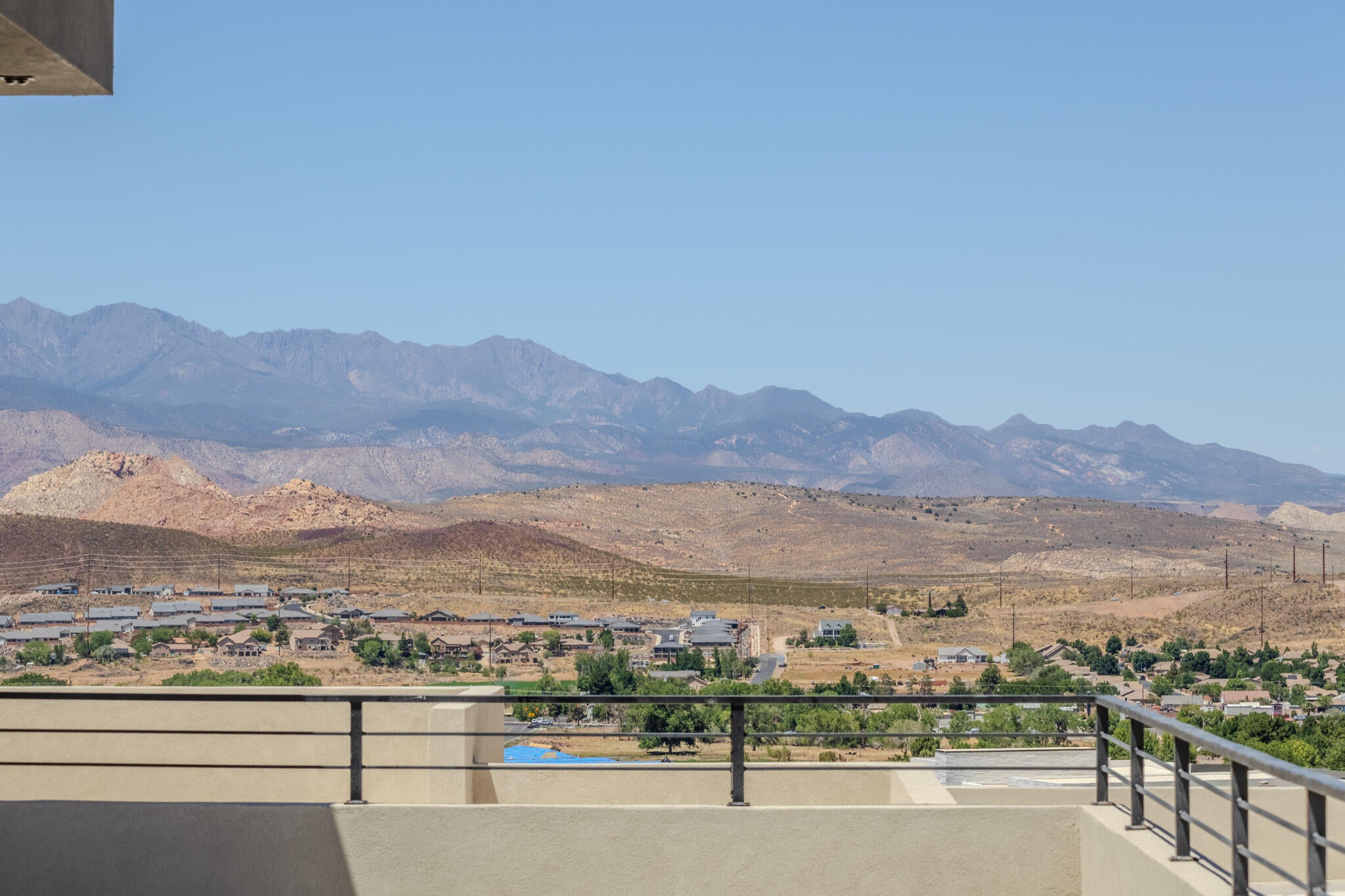 Expansive mountain and desert landscape from a balcony featuring a light-colored stucco wall and dark metal railings