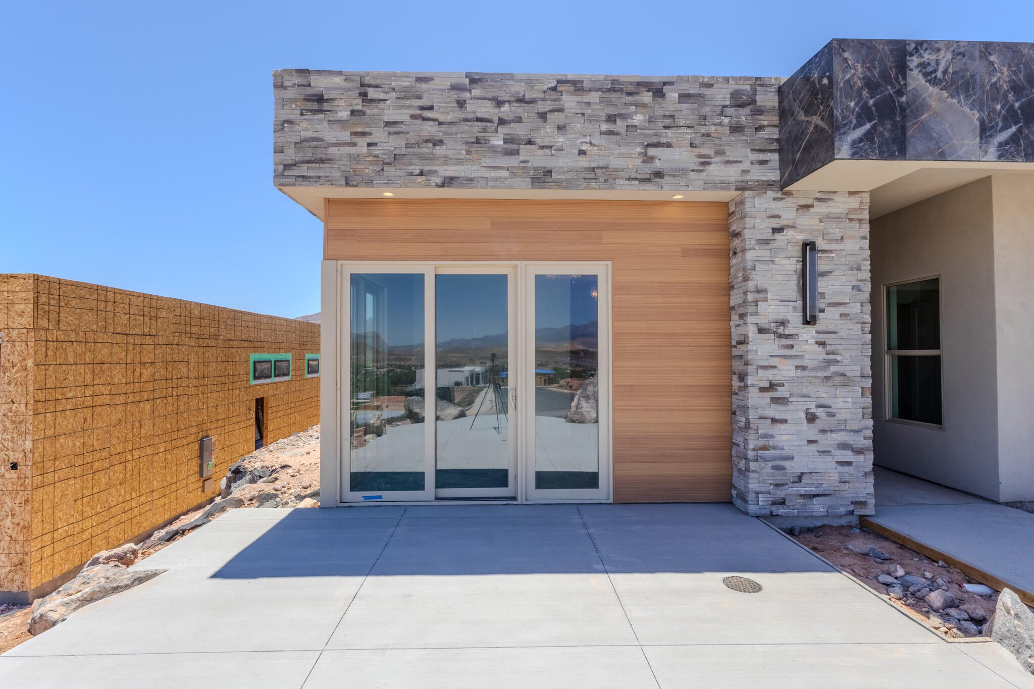 Contemporary exterior featuring stacked stone accents, wood-finish siding, and a large sliding glass door