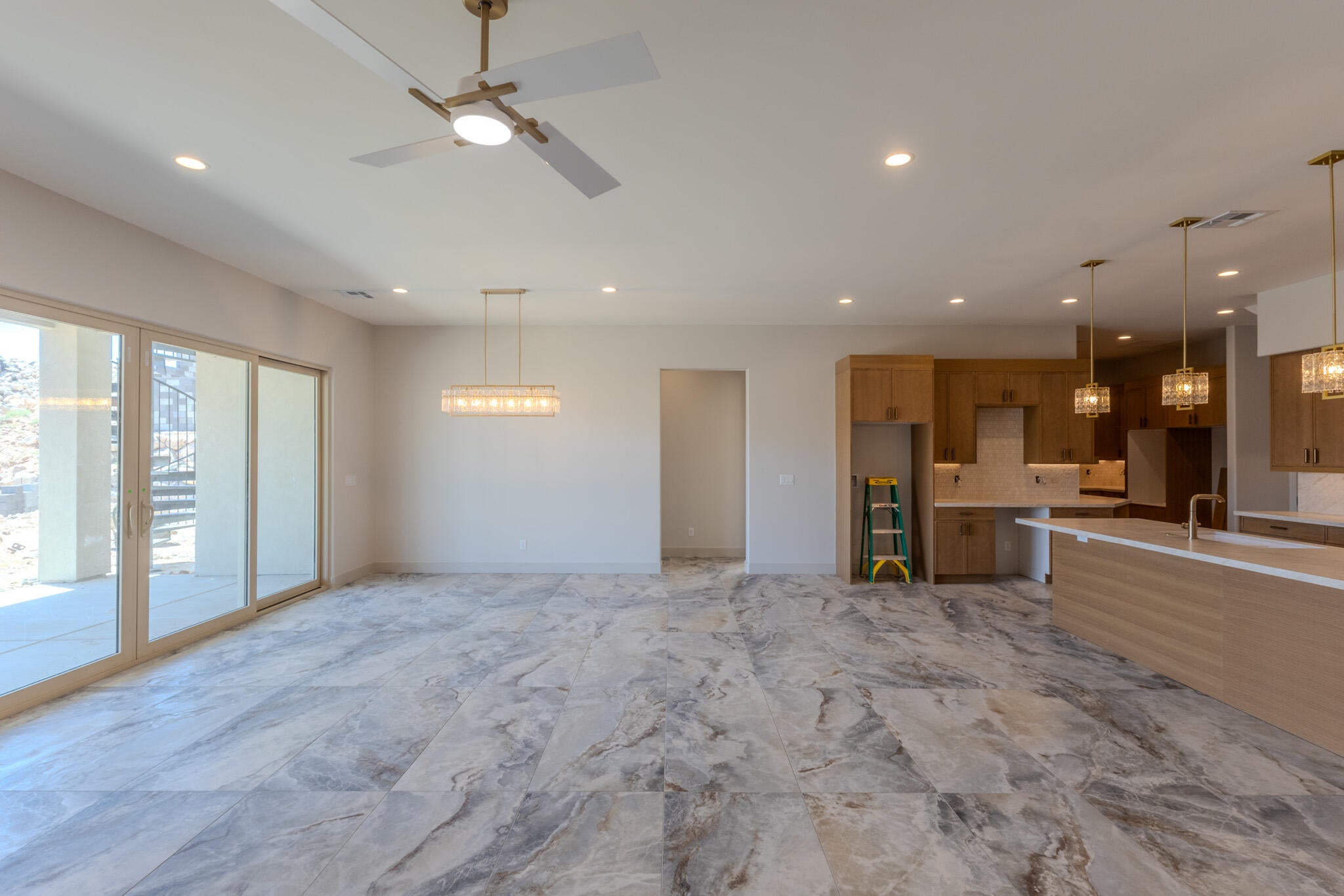 Spacious open-concept living area featuring large format tile flooring, a contemporary ceiling fan, and a linear chandelier