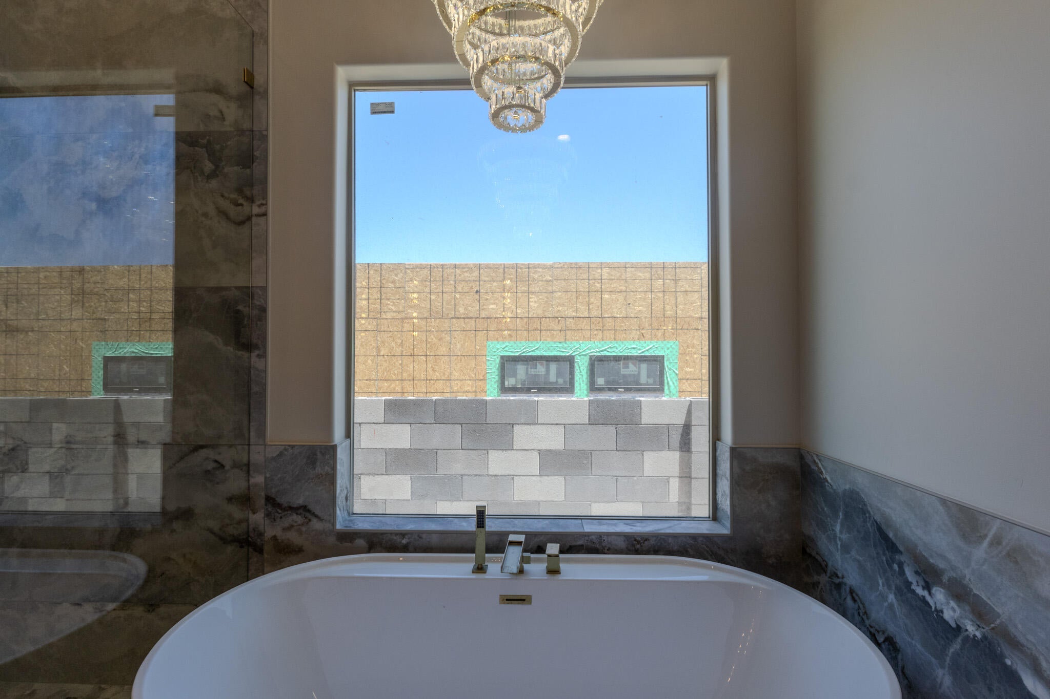 Freestanding soaking tub with polished chrome fixtures, set against a window with a chandelier overhead