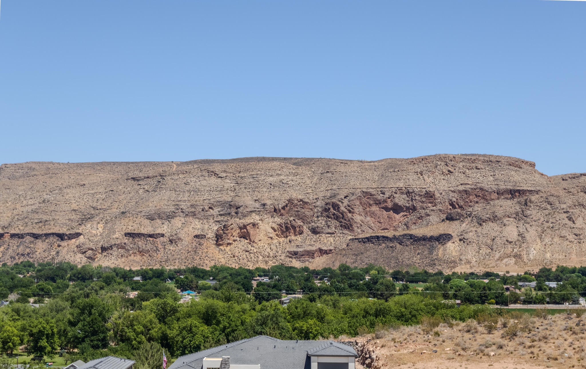 Expansive desert mountain backdrop with distant green foliage and residential rooftops