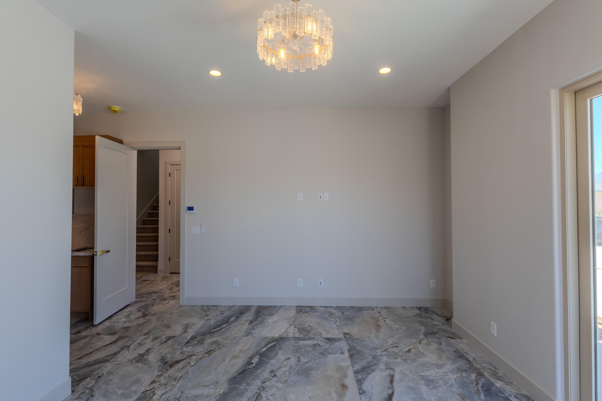 Spacious room featuring large format stone-finish flooring, a modern chandelier, recessed lighting, and a glass-paneled door