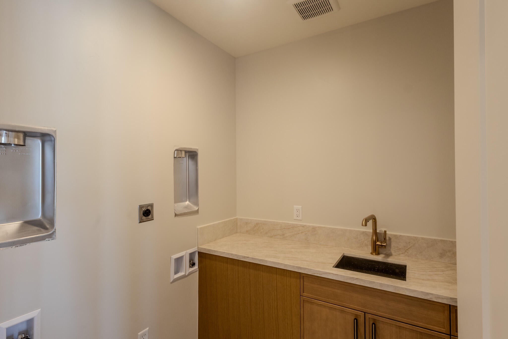 Laundry area featuring a built-in utility sink with brass-finish faucet, stone-finish countertop, wood-finish cabinetry, and connections for laundry appliances