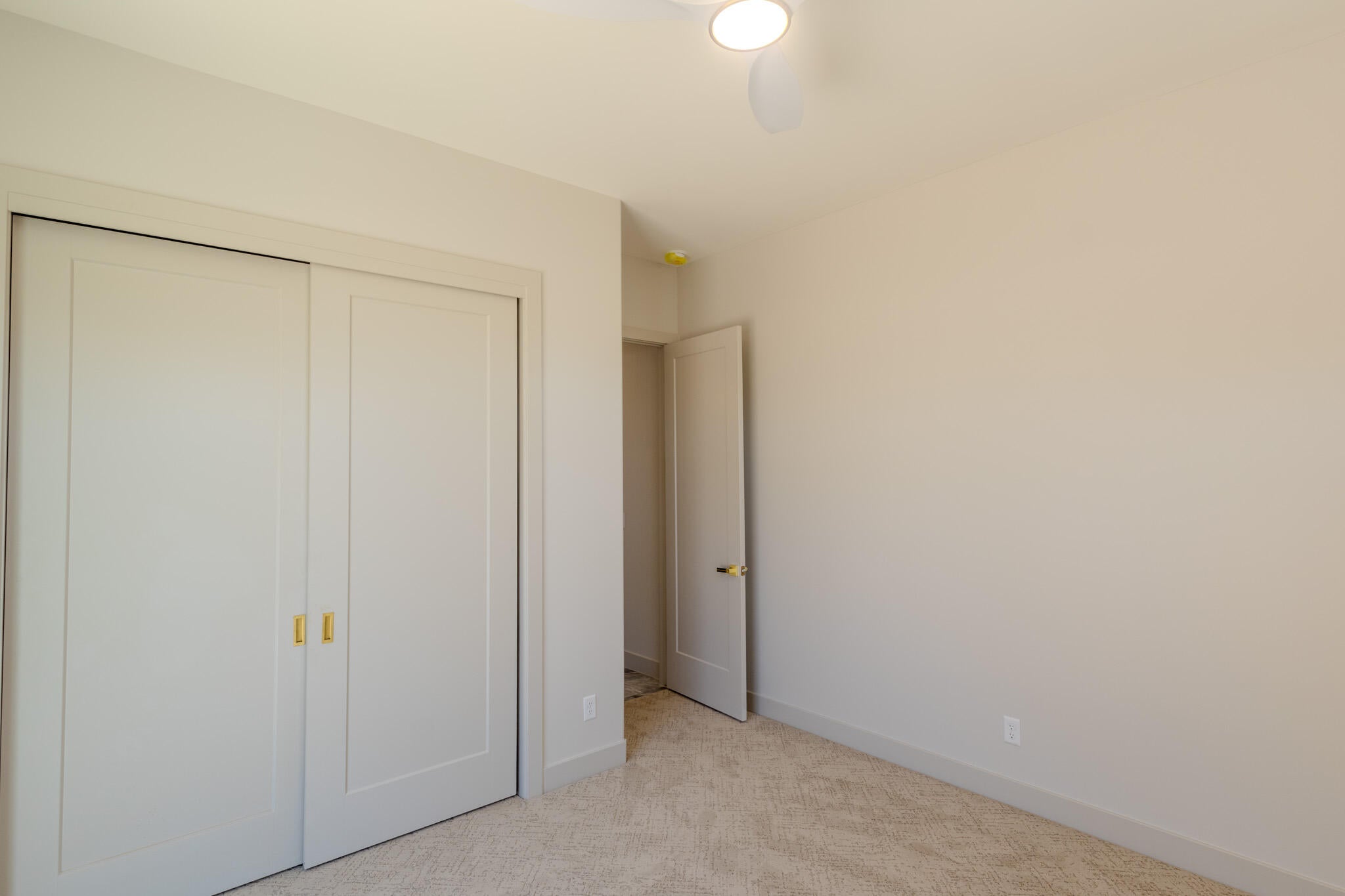 Neutral tone wall paint, carpet flooring, a ceiling fan with integrated lighting, and a closet with dual sliding doors