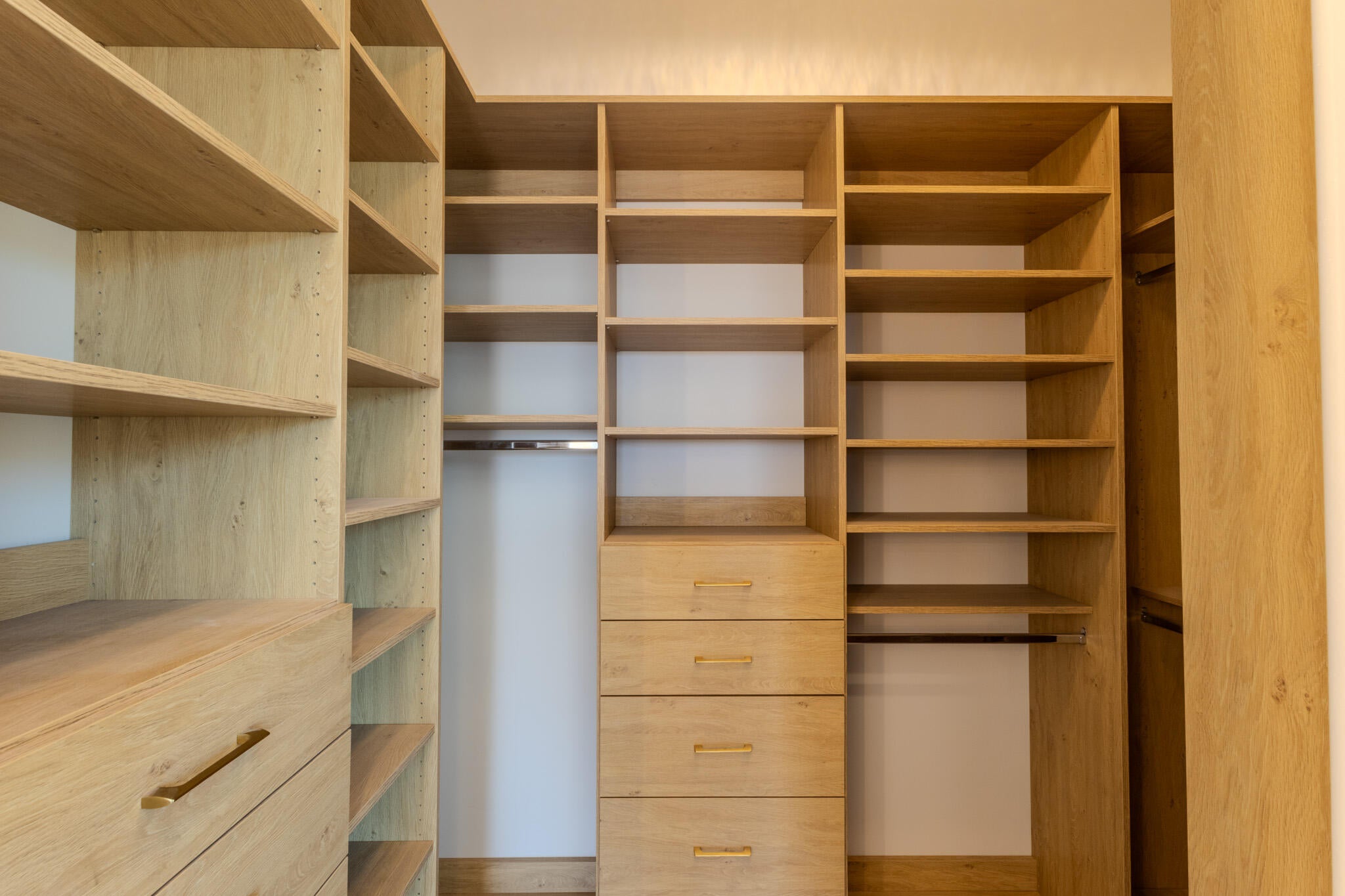 Custom closet system featuring light wood-finish shelving and drawers with gold-tone hardware