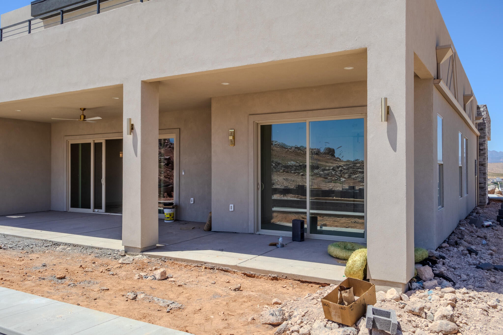 Expansive covered patio featuring a ceiling fan, dual sliding glass doors, exterior sconce lighting, and a stucco exterior finish