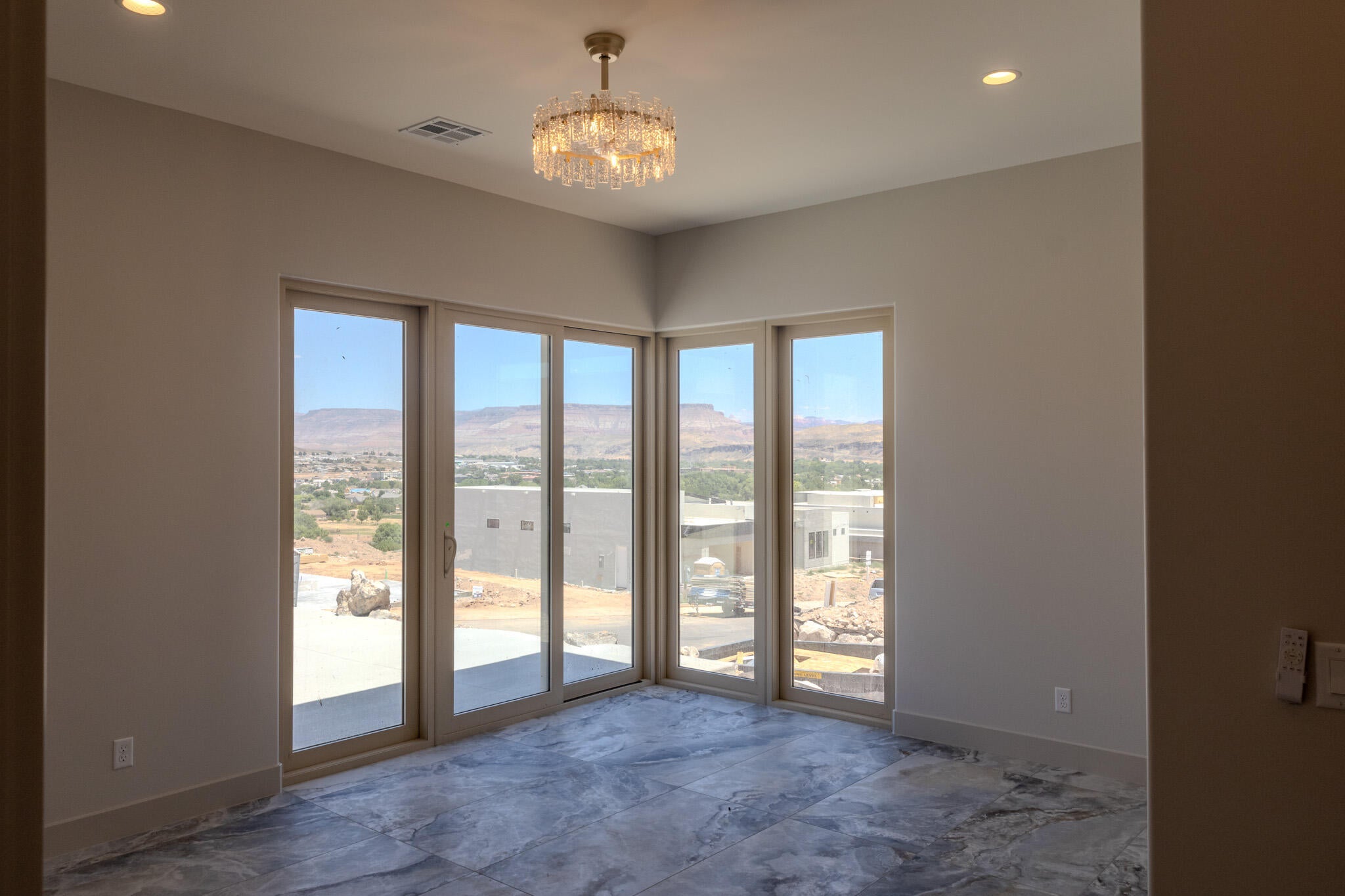 Spacious room featuring floor-to-ceiling sliding glass doors, a decorative crystal chandelier, recessed lighting, and large format stone-finish flooring