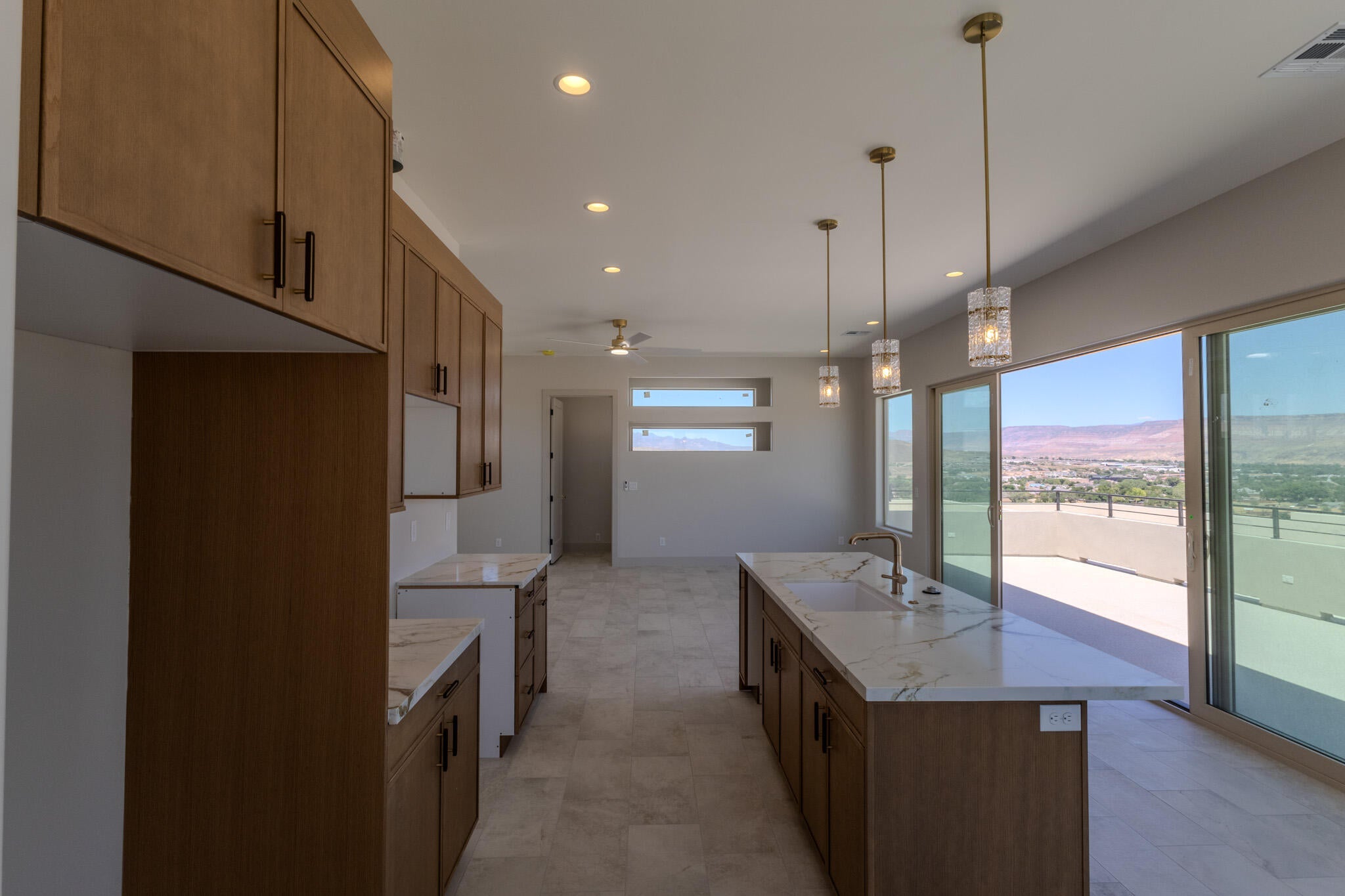 Kitchen featuring full-height wood-finish cabinetry, white countertops with veining, a large center island with integrated sink, recessed lighting, and three pendant light fixtures