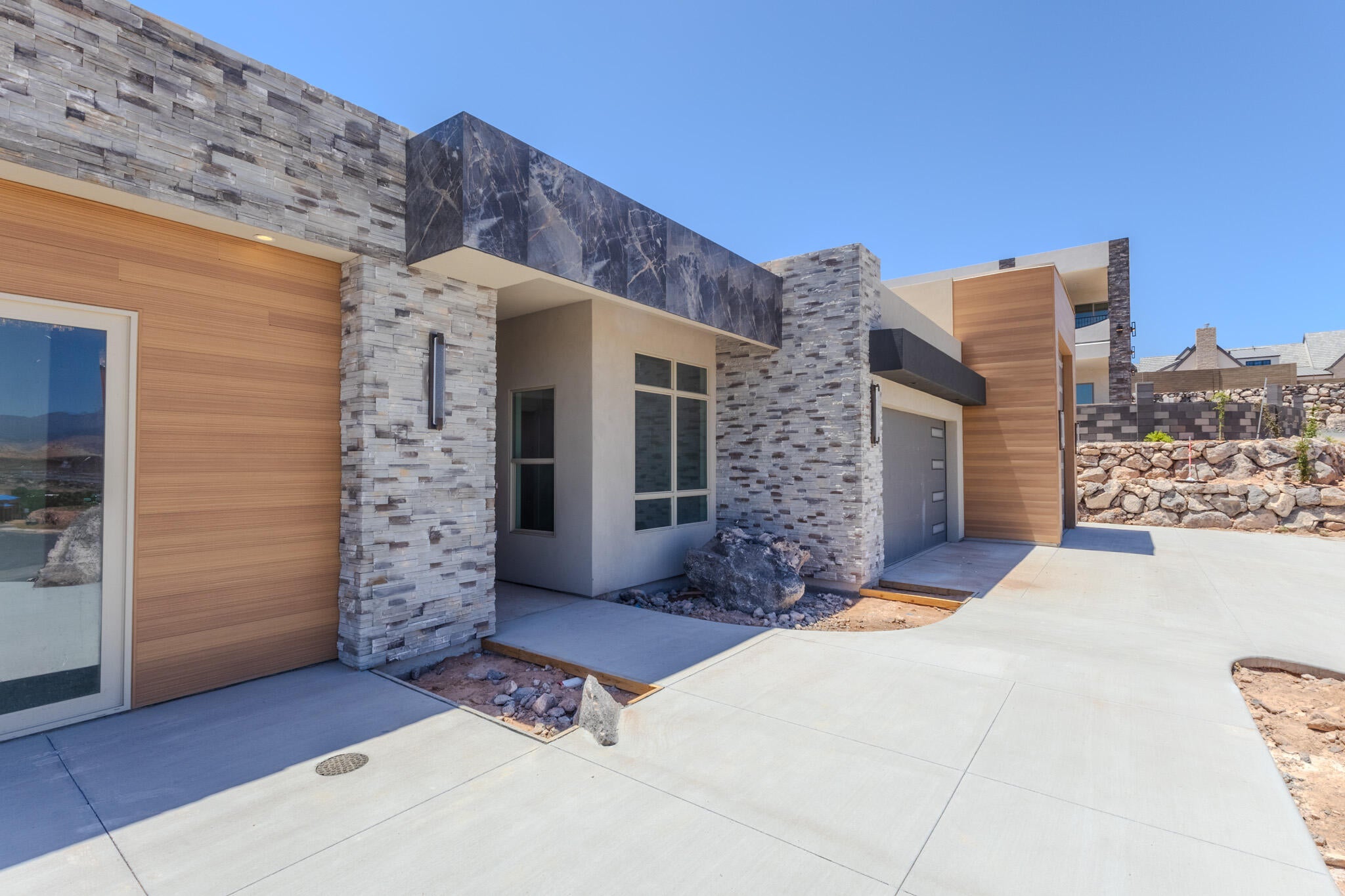 Contemporary exterior featuring stone veneer accents, wood-finish siding, a dark marble-patterned overhang, and a modern garage door