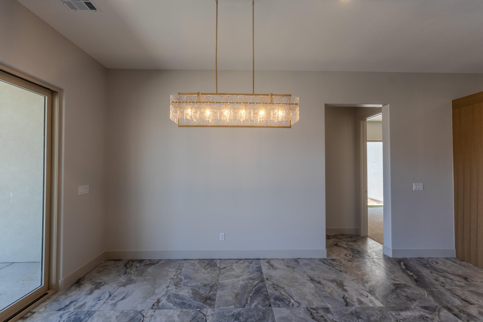 Spacious room featuring large format marble-look tile flooring, a modern linear chandelier with textured glass, and a large glass sliding door