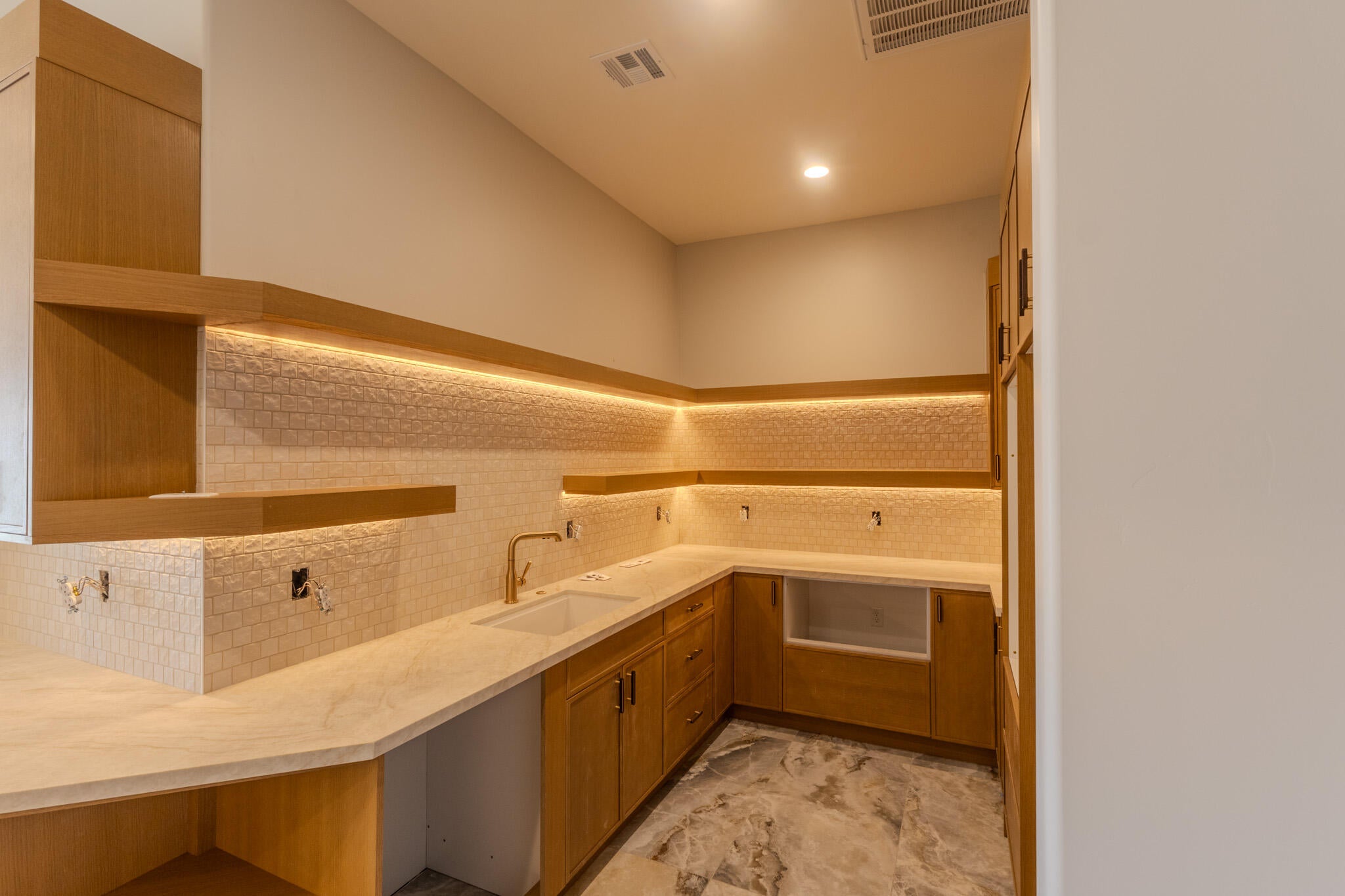 Custom cabinetry with integrated shelving, under-cabinet lighting, a built-in sink, stone-finish countertops, and patterned tile backsplash
