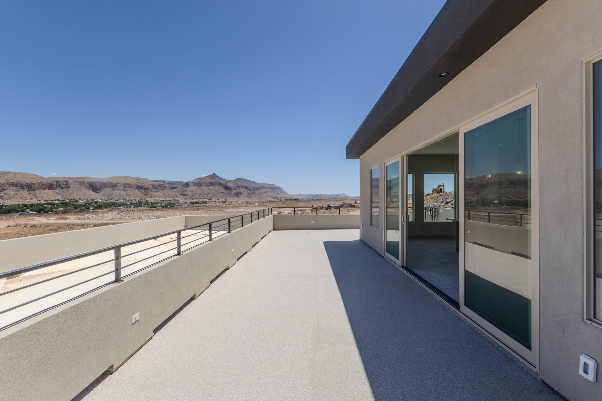 Expansive rooftop deck featuring a stucco exterior with a dark trim, multiple sliding glass doors, contemporary metal railings, and a wide-open desert landscape