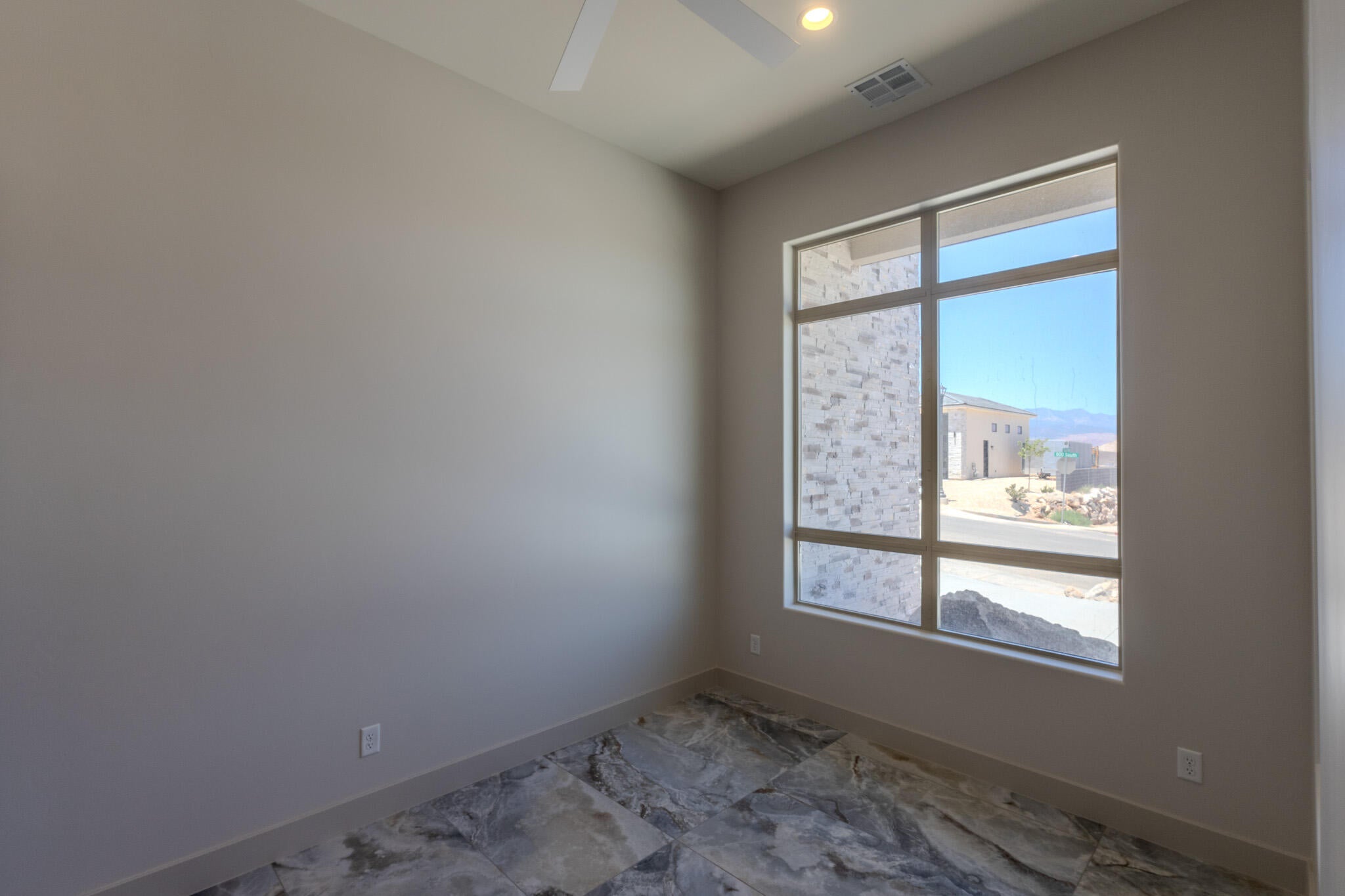 Expansive multi-pane window with a light gray frame, ceiling fan, recessed lighting, and large format stone-look tile flooring
