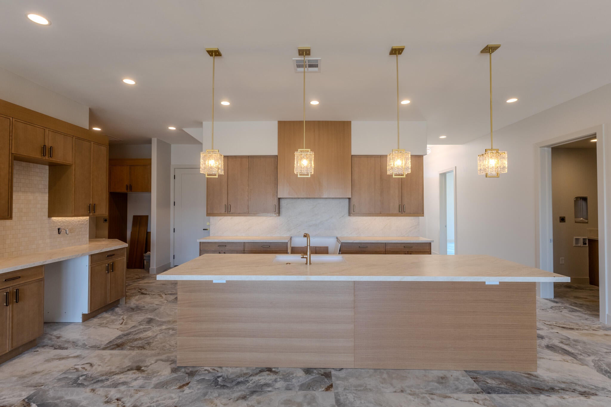 Spacious kitchen featuring a large central island with a light-toned countertop, wood-finish cabinetry, and recessed lighting