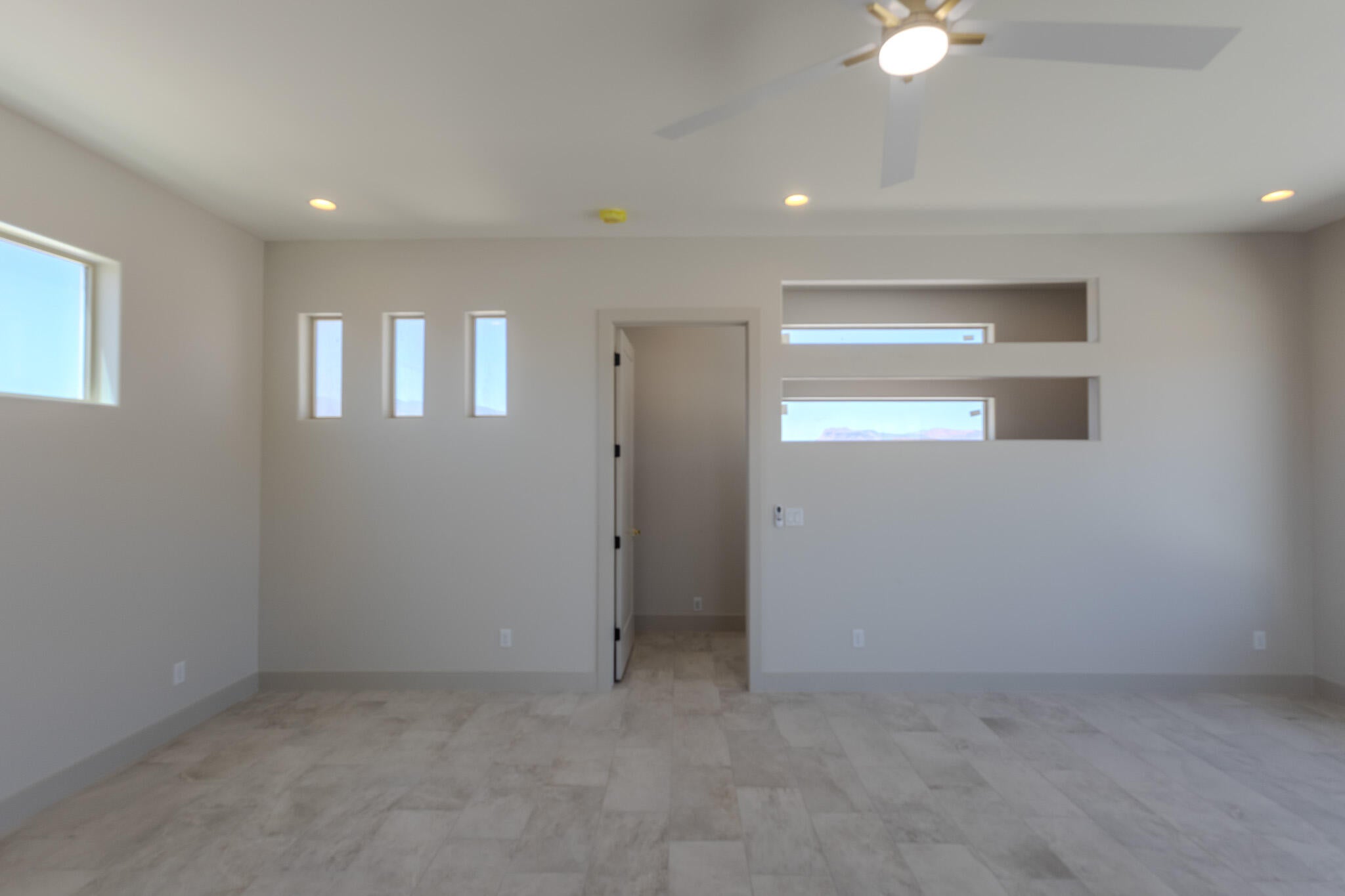 Spacious room featuring light-colored tile flooring, multiple recessed light fixtures, and a ceiling fan