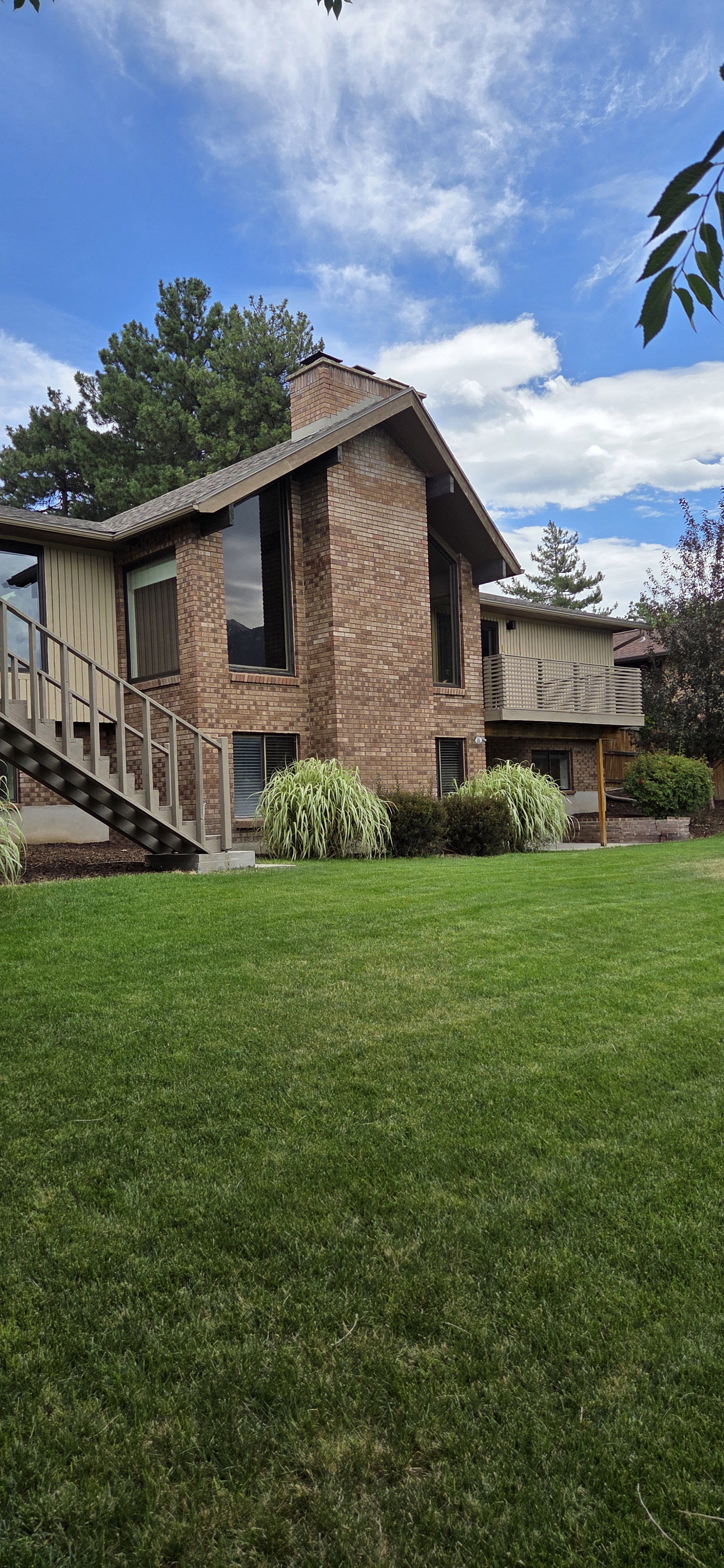 Brick and siding exterior featuring an prominent chimney, large windows, an exterior staircase, and a wood deck