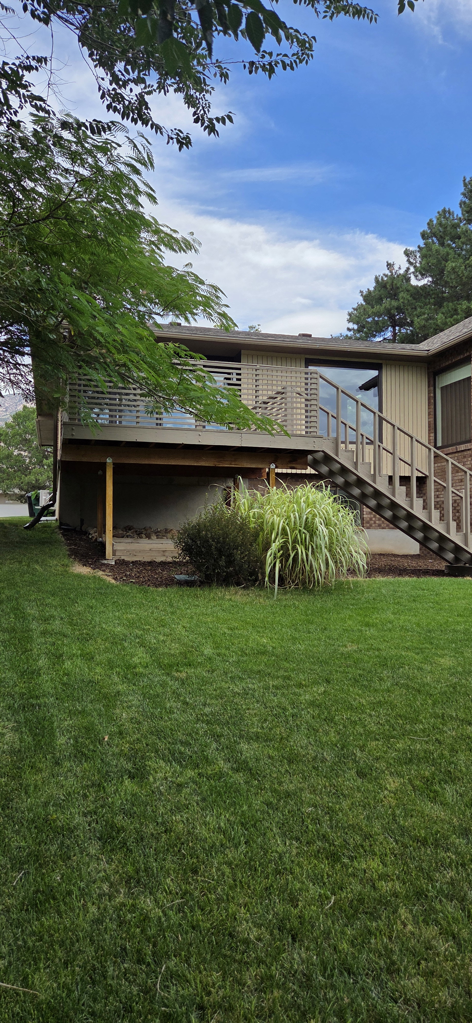 Rear exterior featuring a multi-level deck with slatted railing, exterior staircase, large picture window, and brick facade