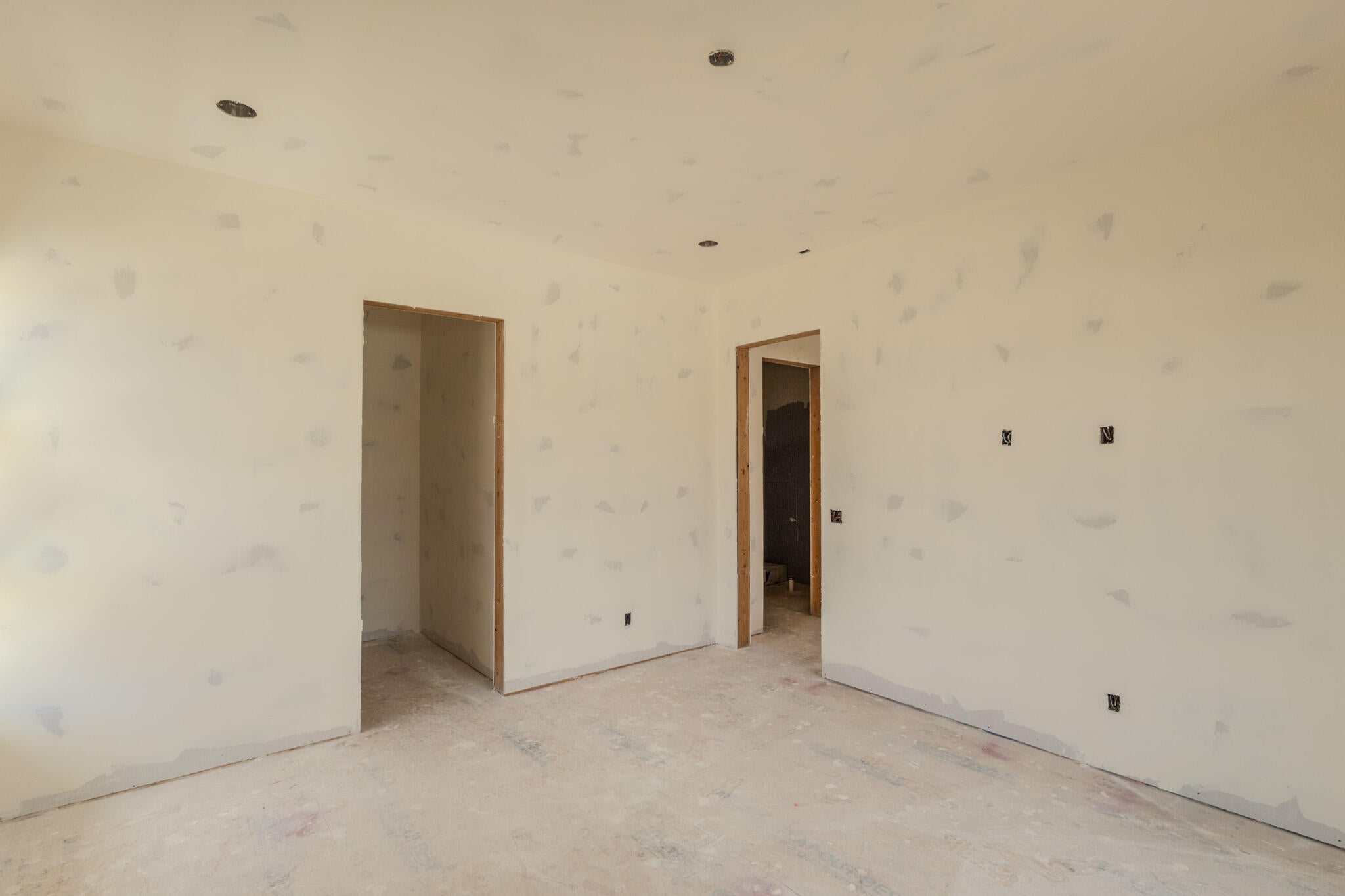 Unfinished interior space featuring recessed ceiling lighting, two open doorways with wood framing, and wall-mounted electrical boxes