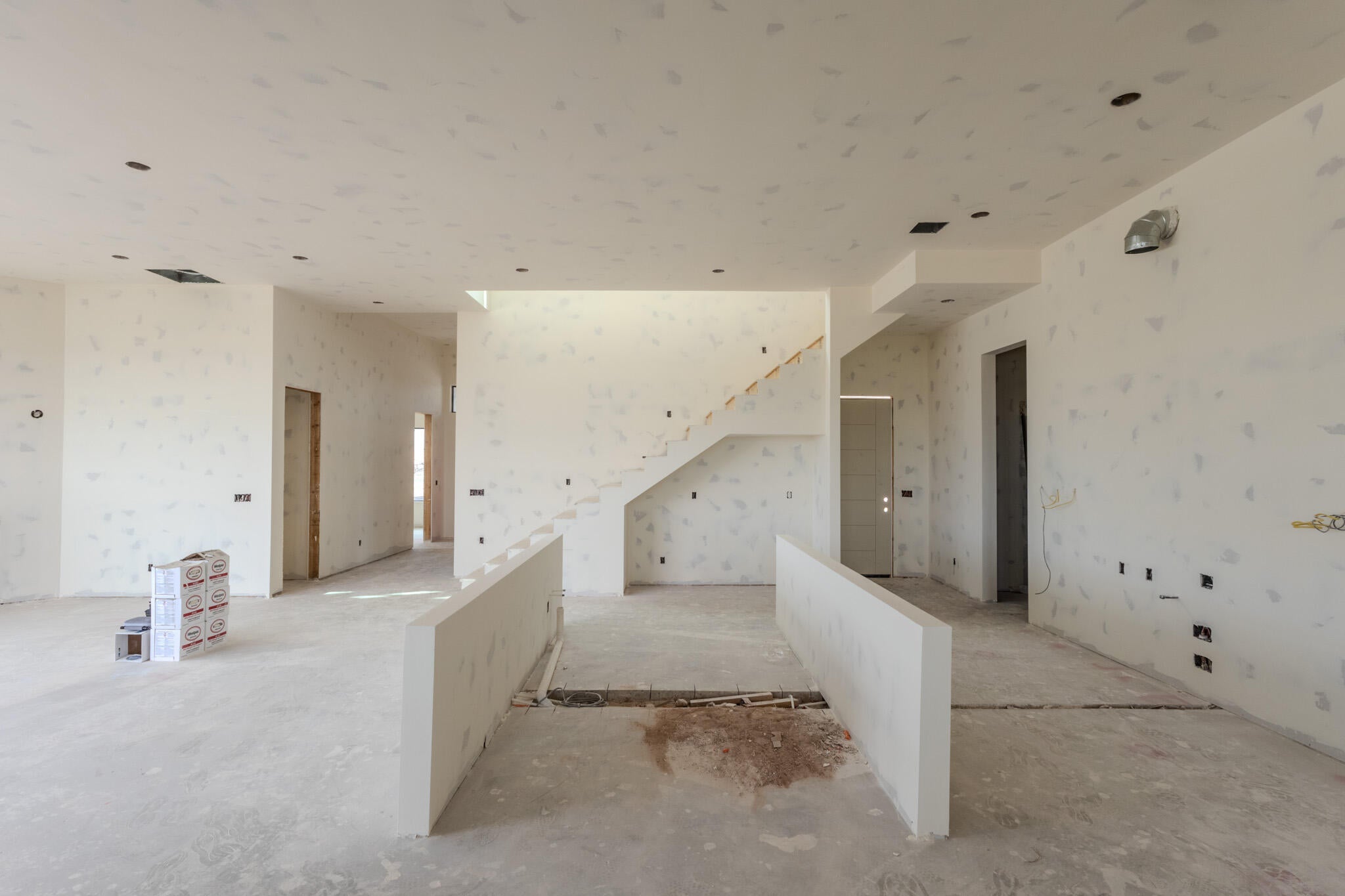 Spacious interior under construction featuring raw concrete flooring, a partial staircase, and multiple doorways