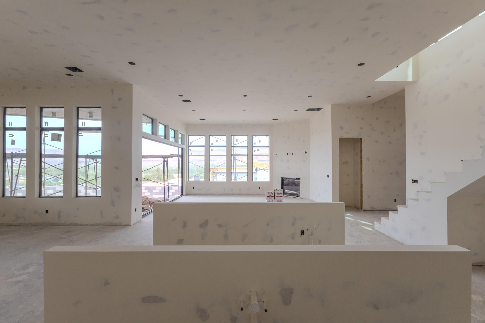 Spacious open-concept interior featuring multiple large windows, recessed ceiling lighting, a built-in fireplace, and a cantilevered staircase