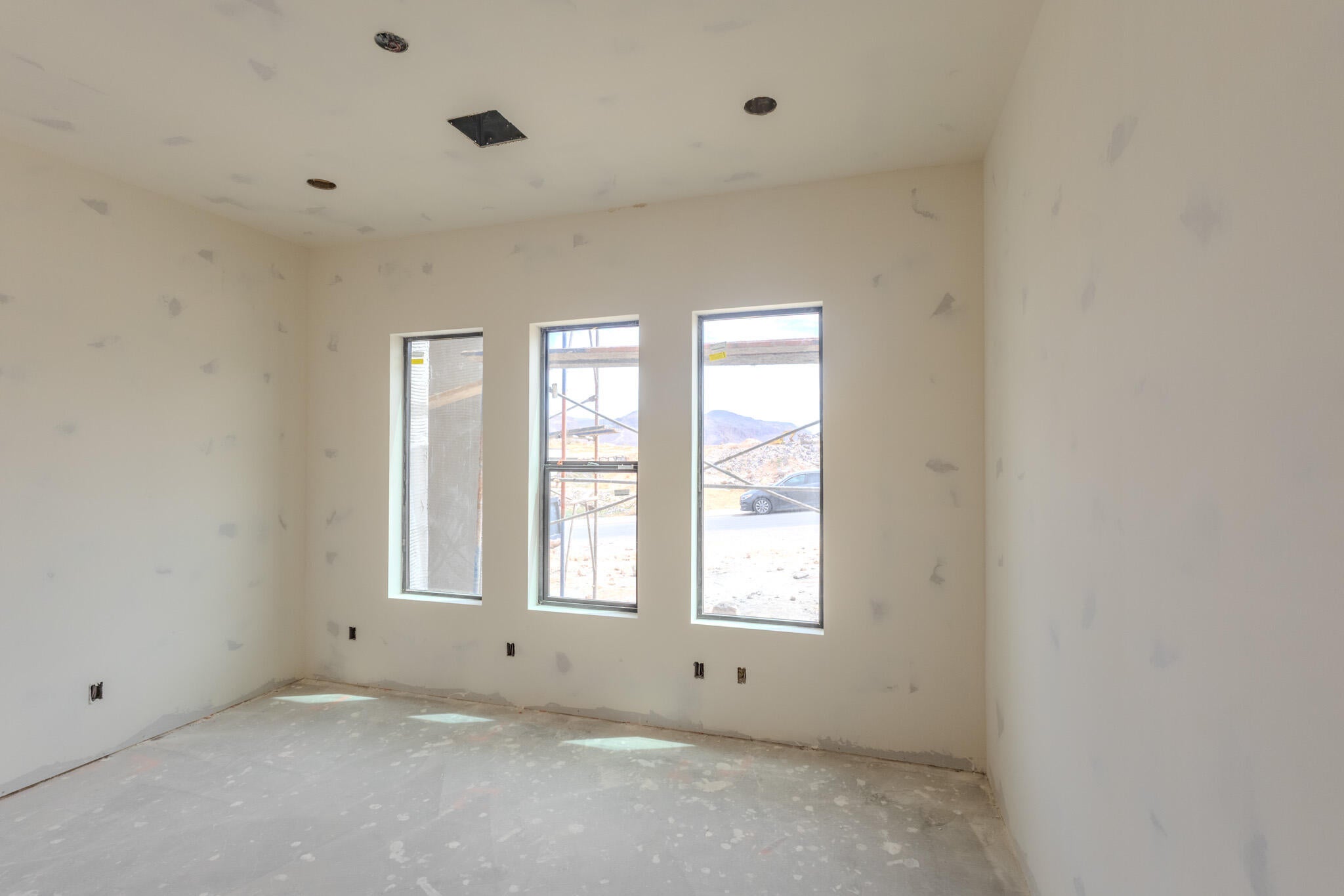 Spacious interior room with three vertical windows, recessed lighting, and a square ceiling vent