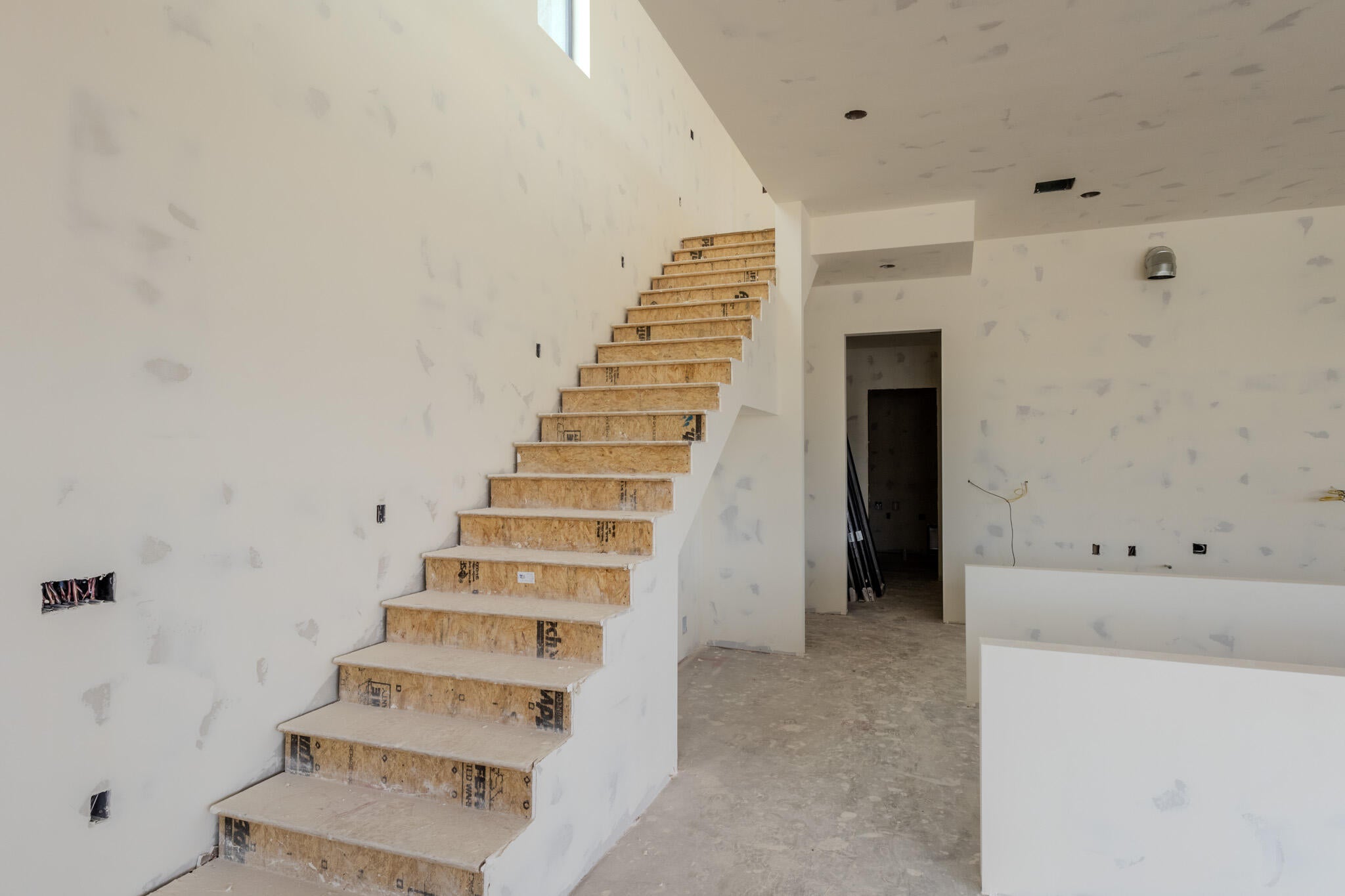 Expansive interior space featuring a tall ceiling and an unfinished wooden staircase