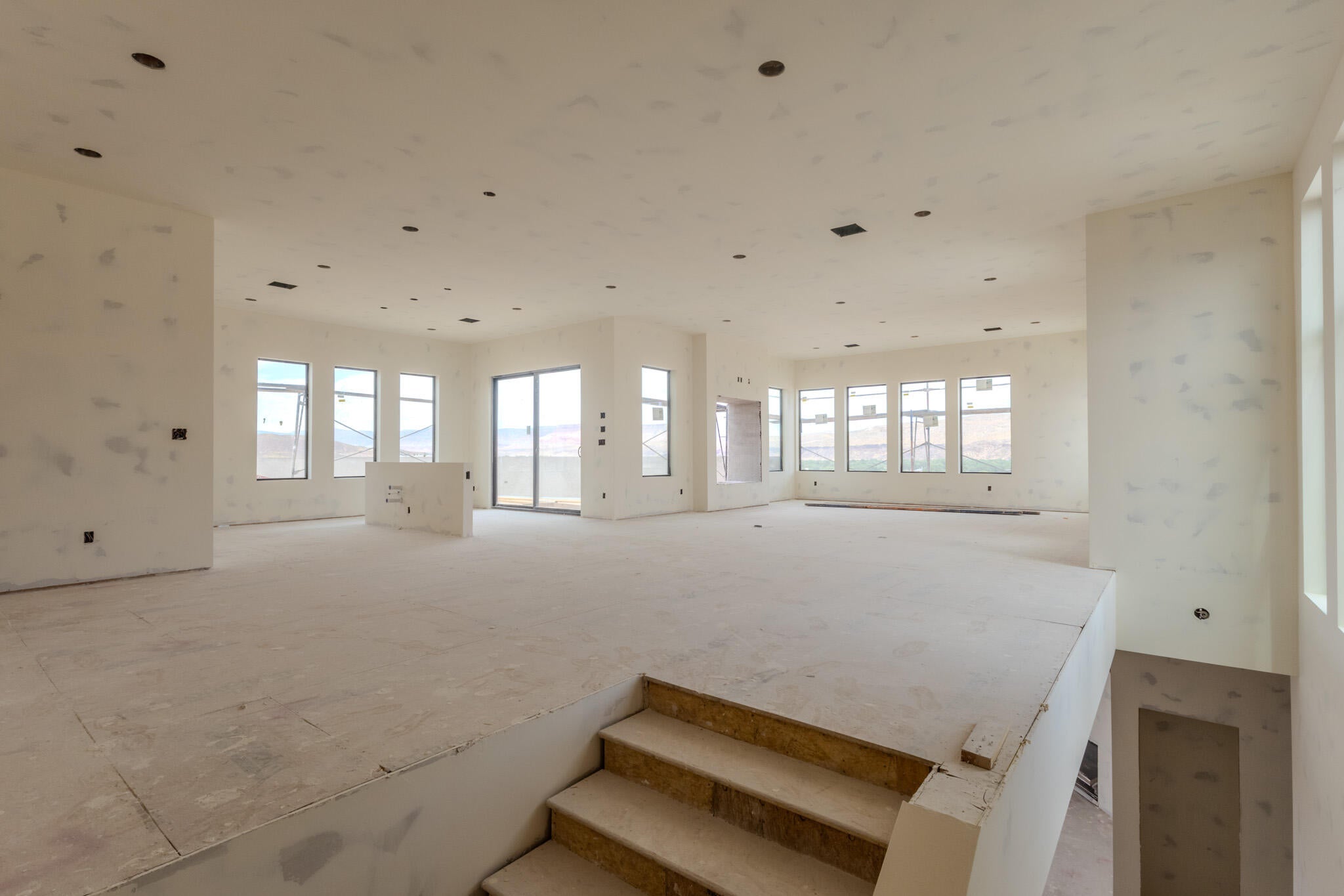 Expansive open-concept living area featuring numerous windows, recessed lighting, a sliding glass door, and an unfinished central island structure
