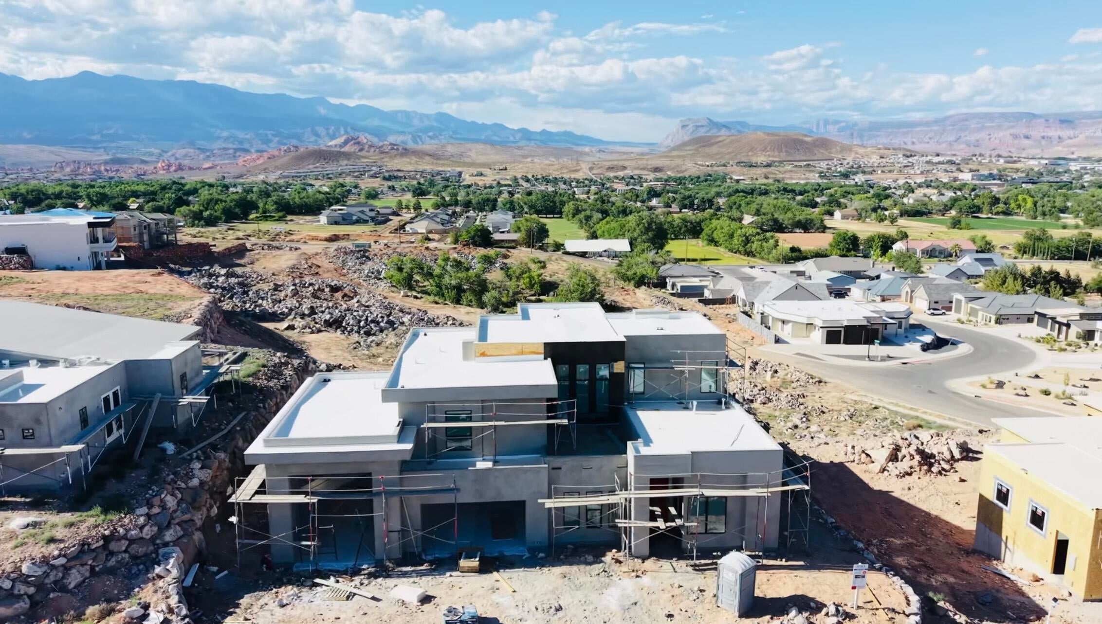 Modern architecture under construction with flat rooflines and multiple windows, set against a backdrop of distant mountains and green valleys