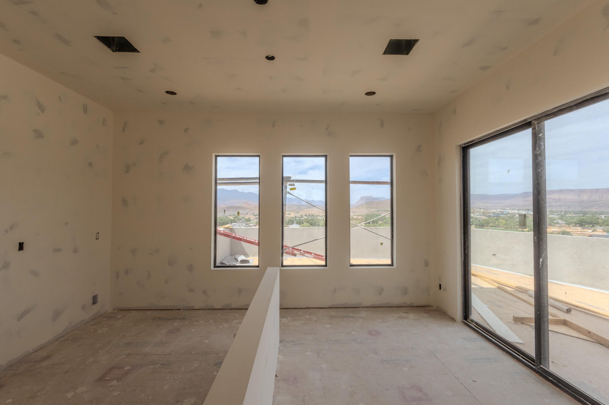 Expansive room featuring a large sliding glass door, three vertical windows, recessed ceiling lighting, and a partial wall divider