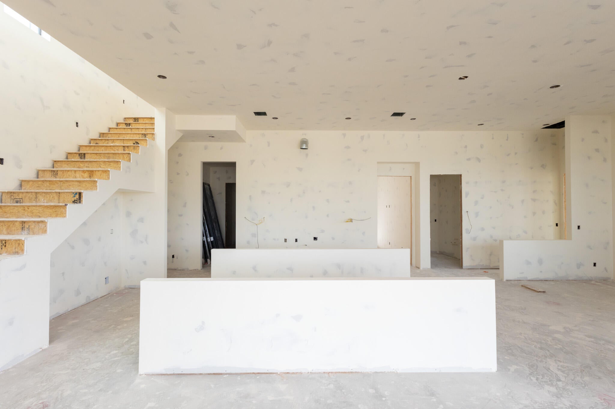 Spacious interior with exposed staircase framing, unfinished drywall, and concrete flooring