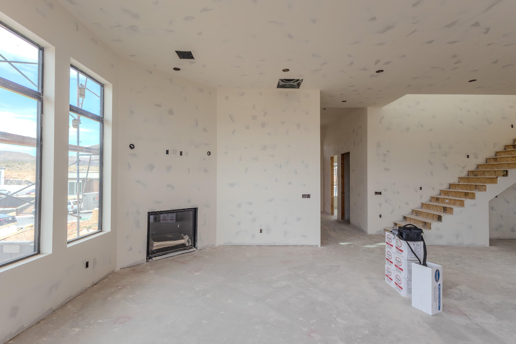 Open-concept living space with large windows, a built-in fireplace, recessed lighting, and an exposed staircase