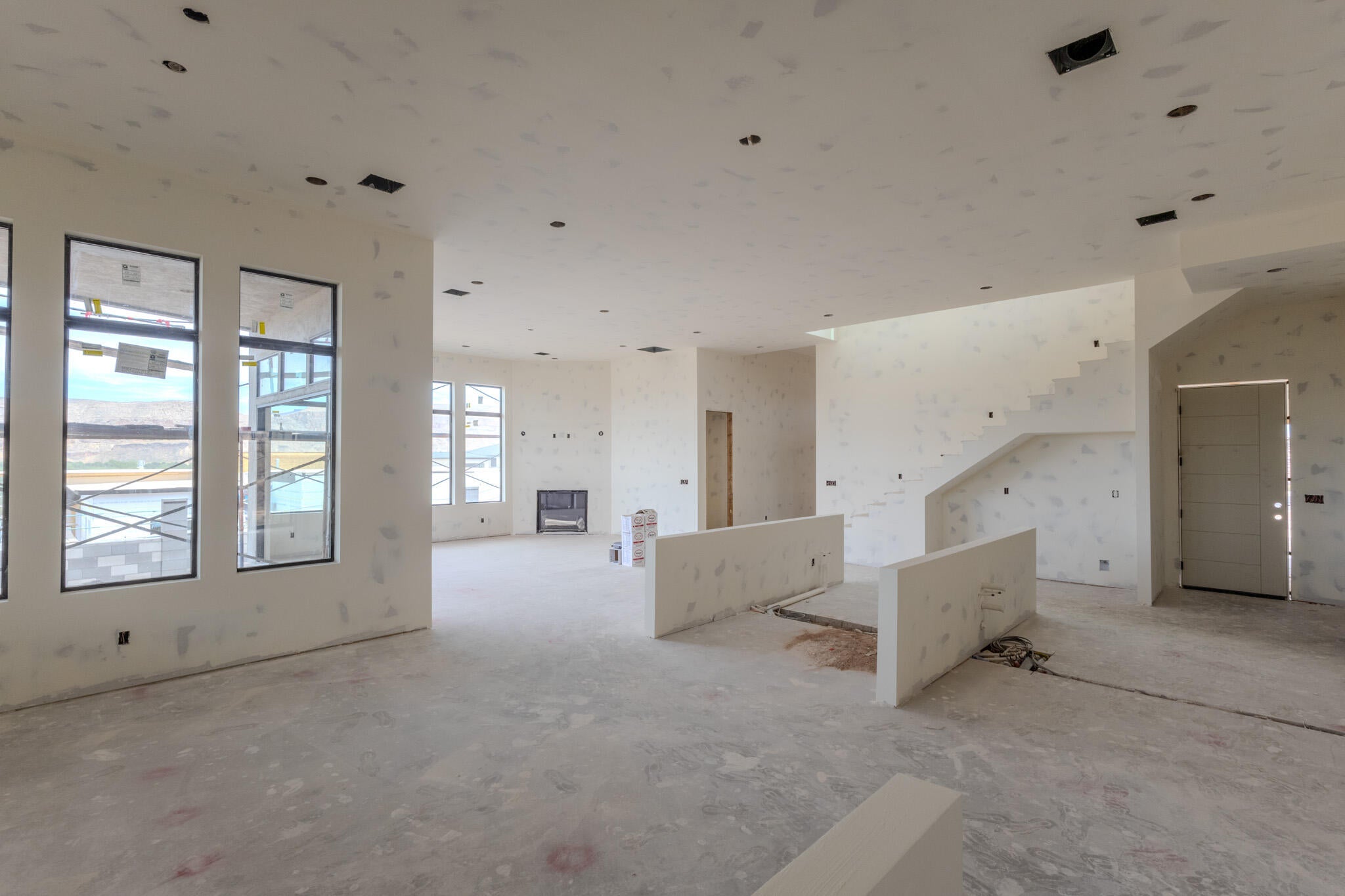 Open-concept living area featuring a large window array, a visible staircase, a modern entry door, and recessed lighting