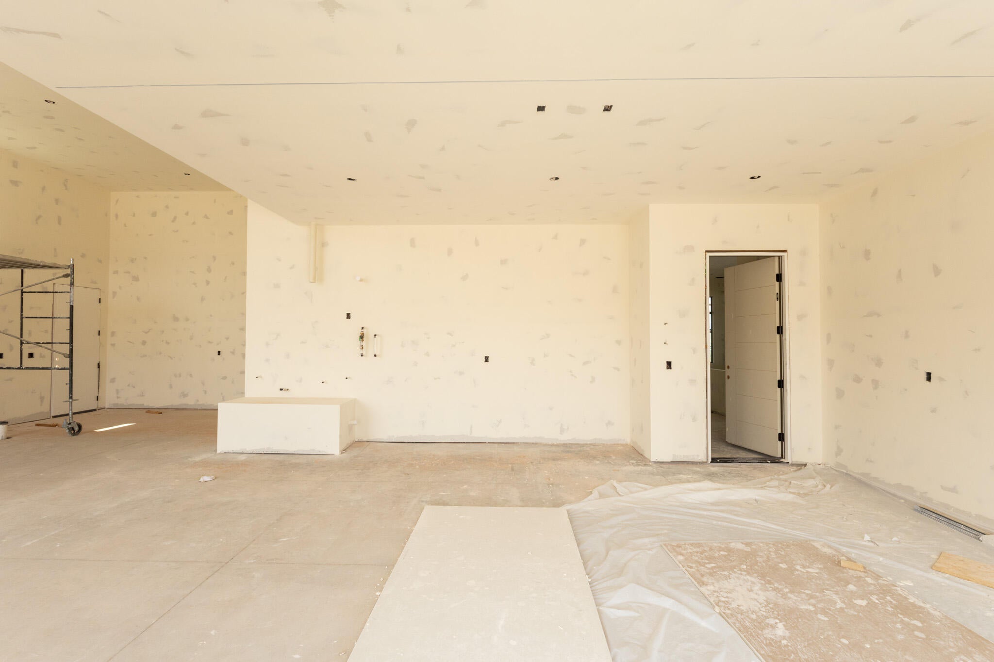 Spacious interior room with an unfinished concrete floor, recessed ceiling lighting, and a modern paneled door