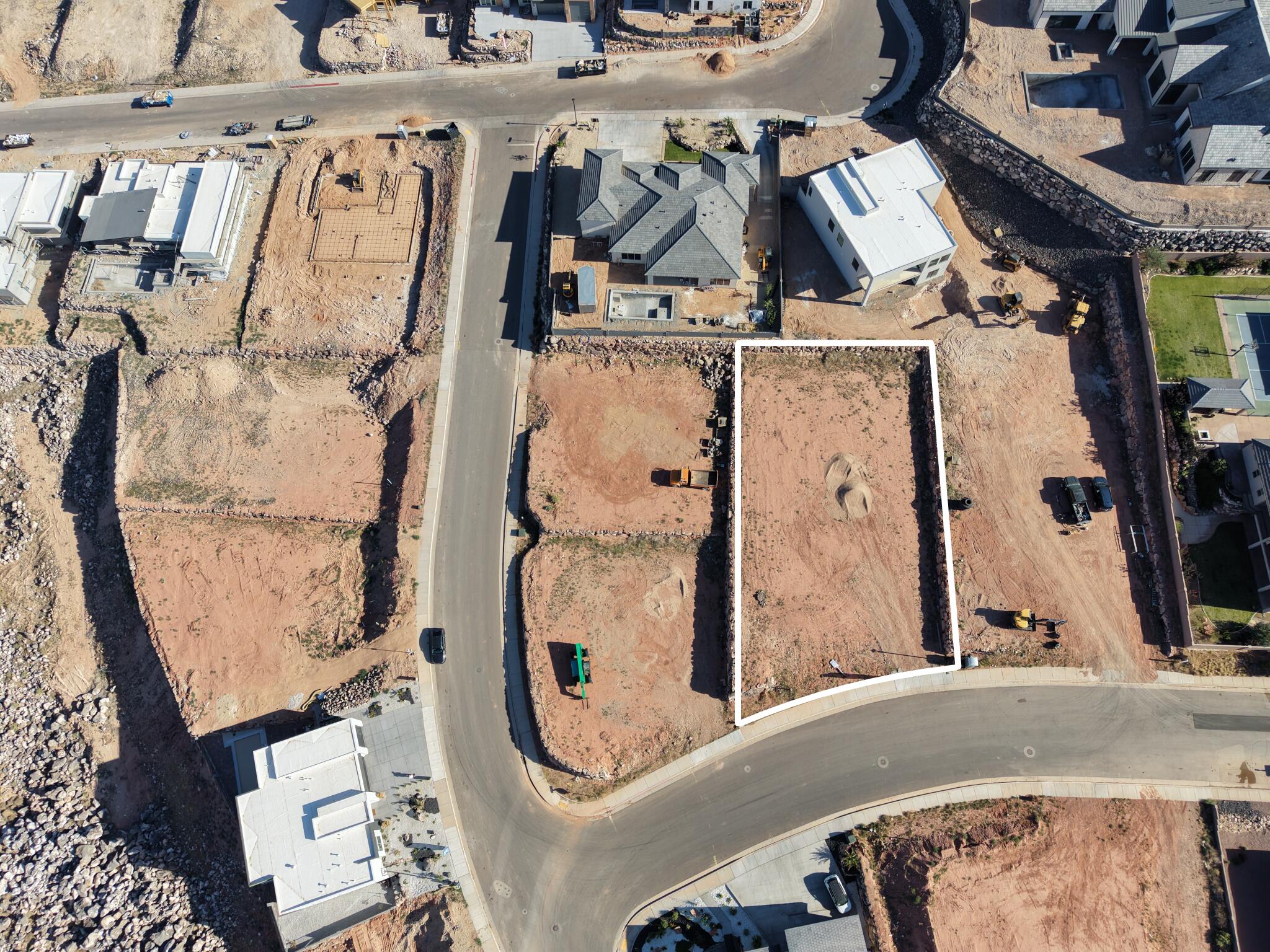 Two distinct, level building lots outlined in white, featuring red earth and situated on a paved street