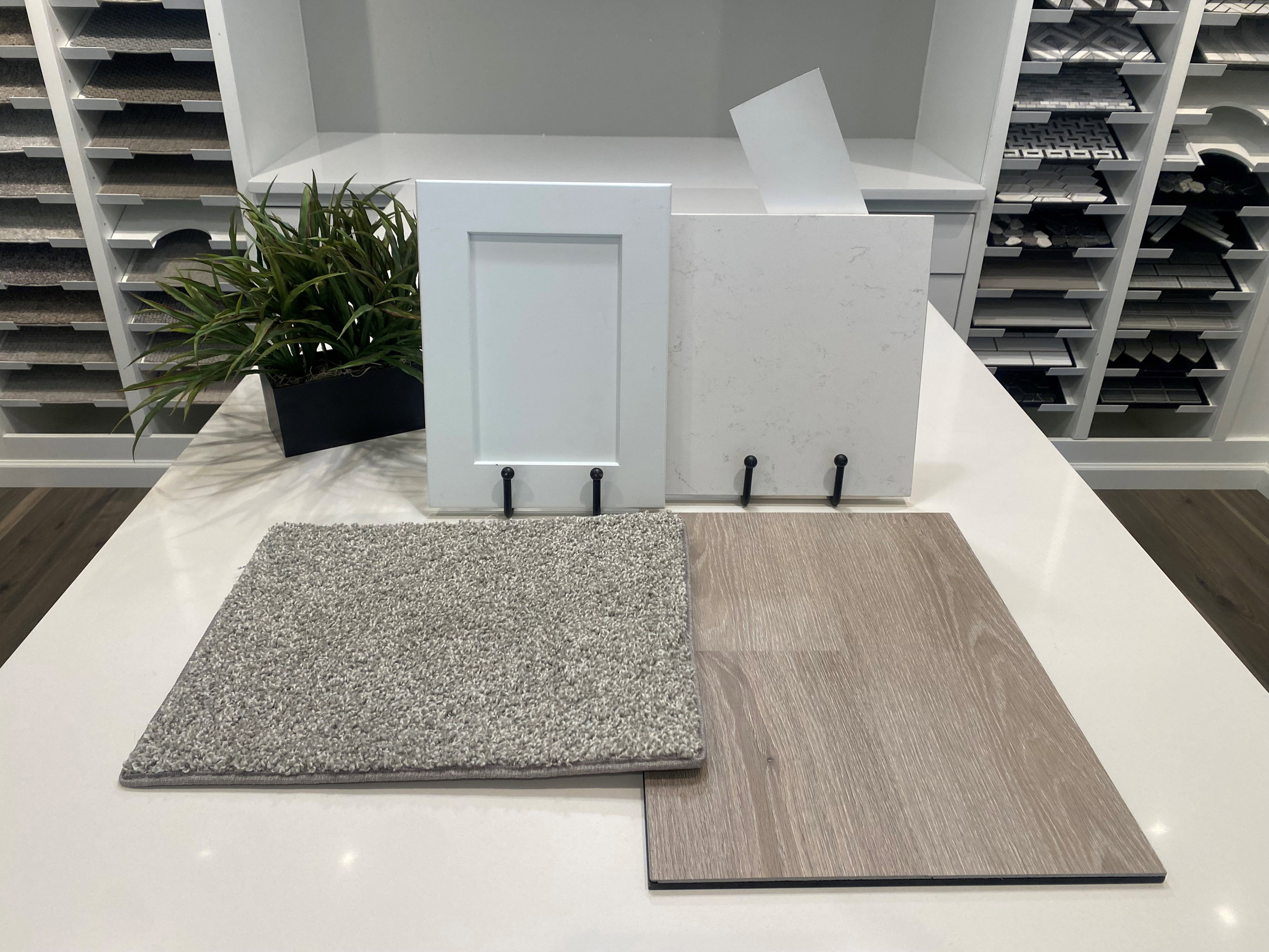 Interior Color Samples: White shaker-style cabinet panel, light-toned stone-finish countertop sample, grey textured carpet sample, and wood-finish flooring sample