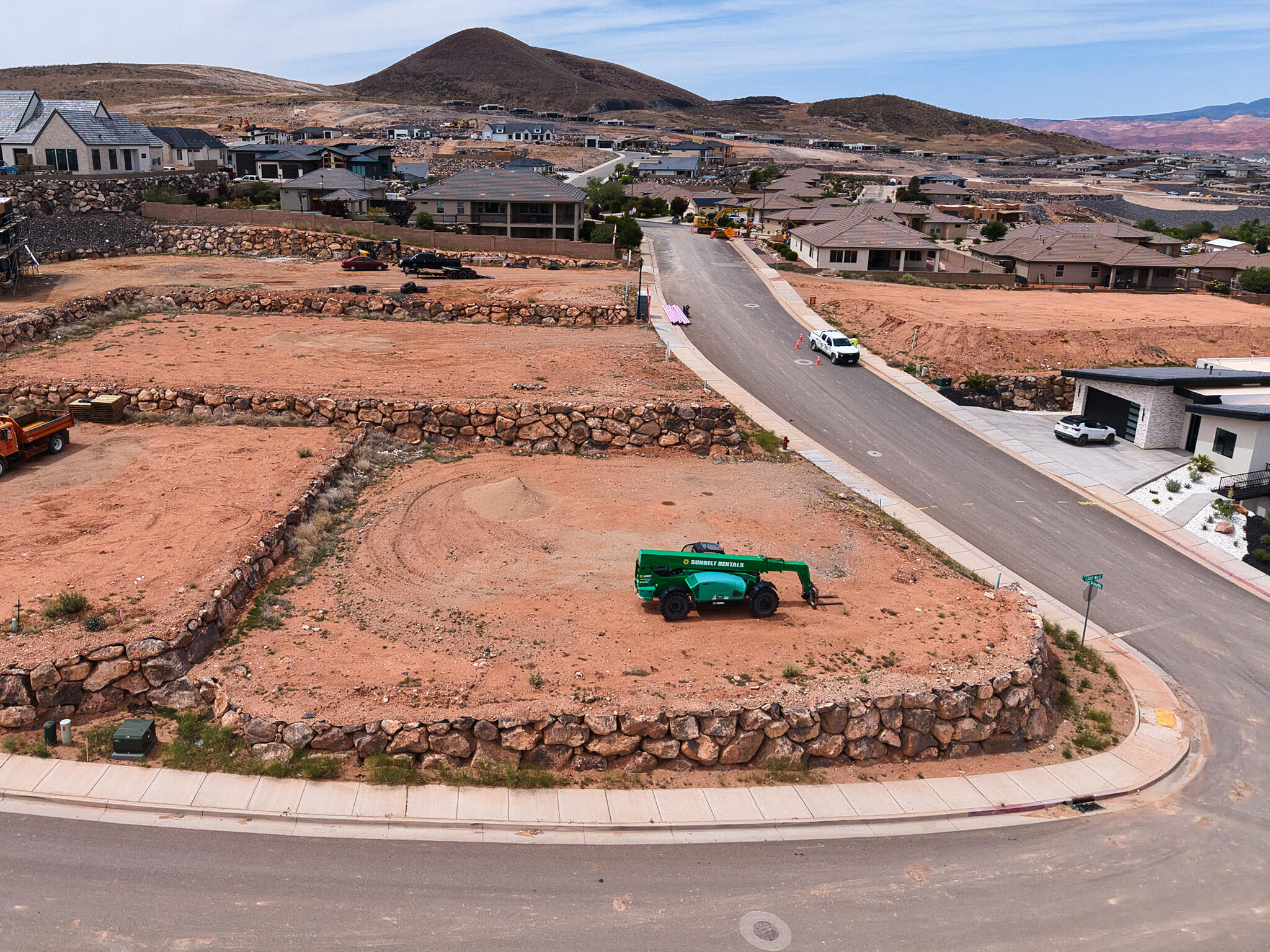 Graded residential lot featuring a paved road frontage, concrete sidewalks, and a rock retaining wall