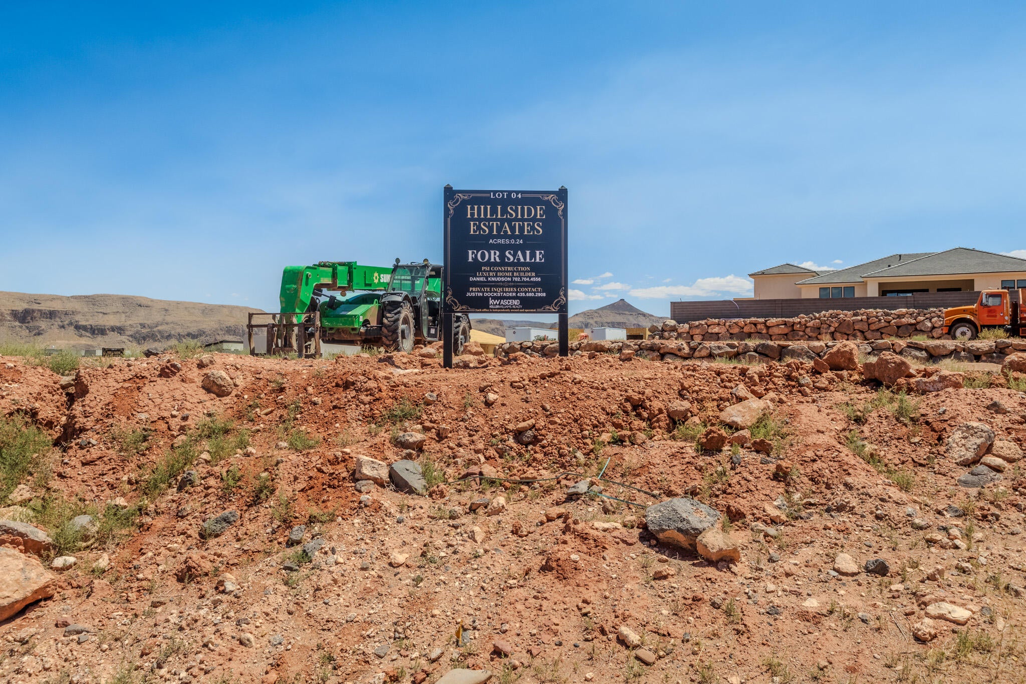 Residential lot featuring a "Hillside Estates For Sale" sign, expansive undeveloped terrain, distant structures, and a clear sky