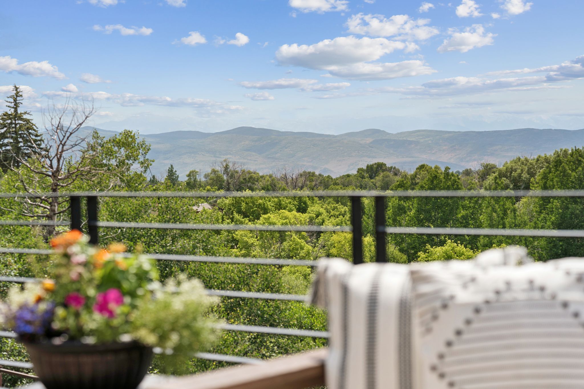 Outdoor balcony featuring a metal railing system, lush green foliage, and distant mountain scenery