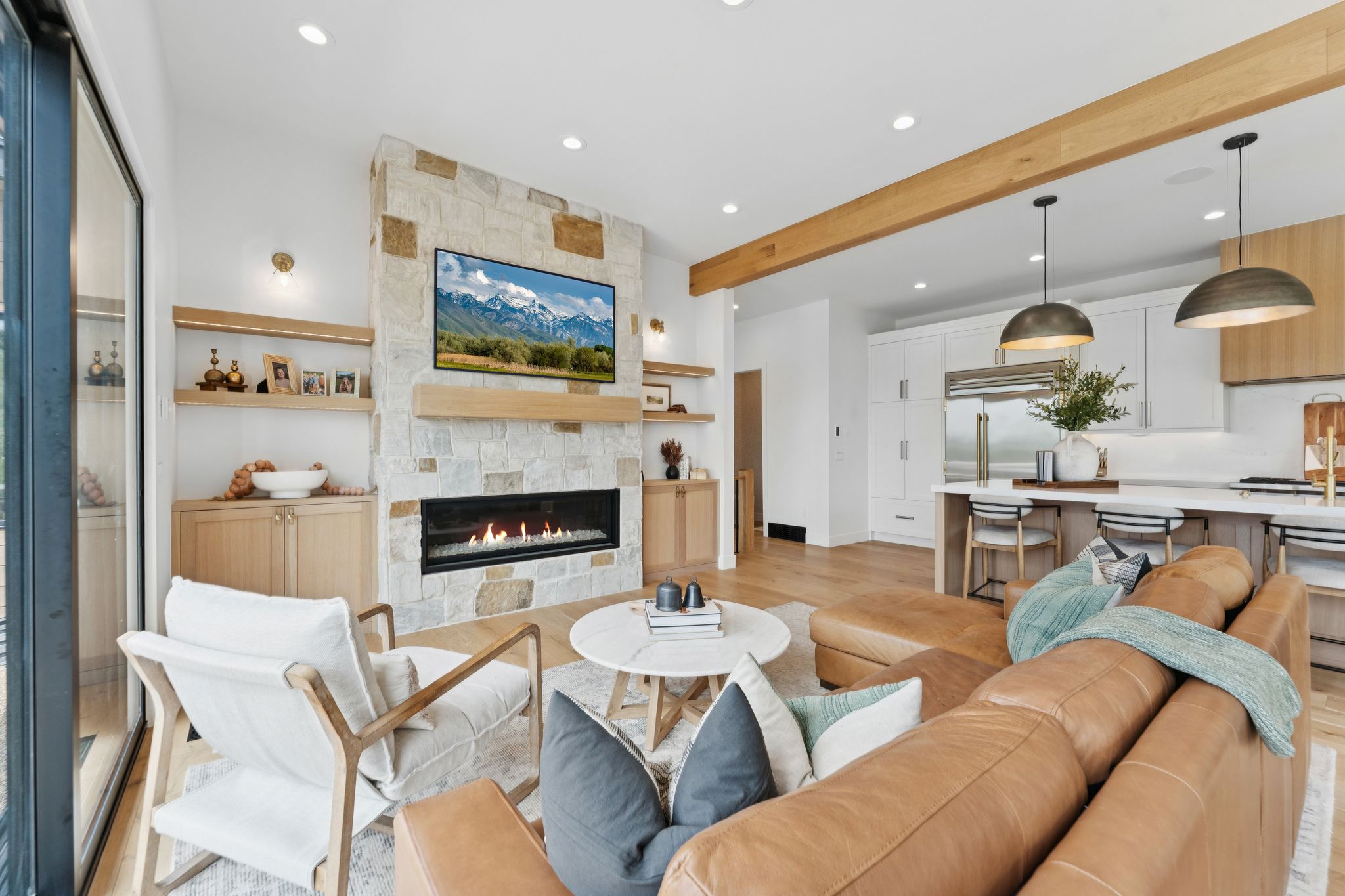 Open-concept living area featuring a stone-clad fireplace with a linear firebox, natural wood-finish mantel, and integrated built-in cabinetry with open shelving