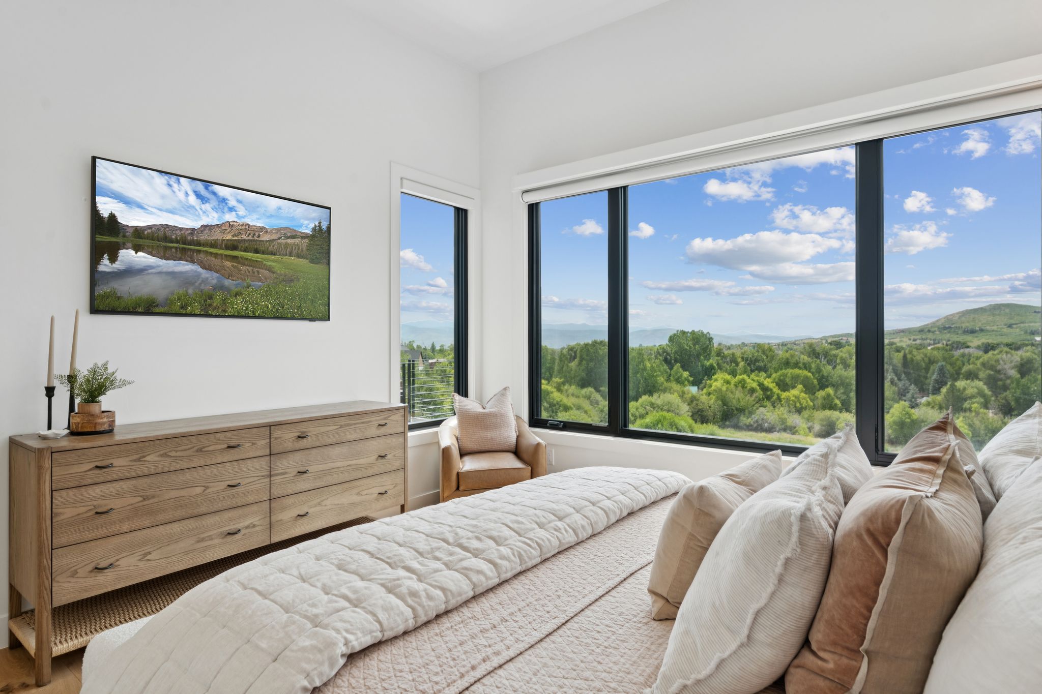 Expansive window wall with black framing, high ceilings, light wood-finish flooring, and a large wood-finish dresser with six drawers