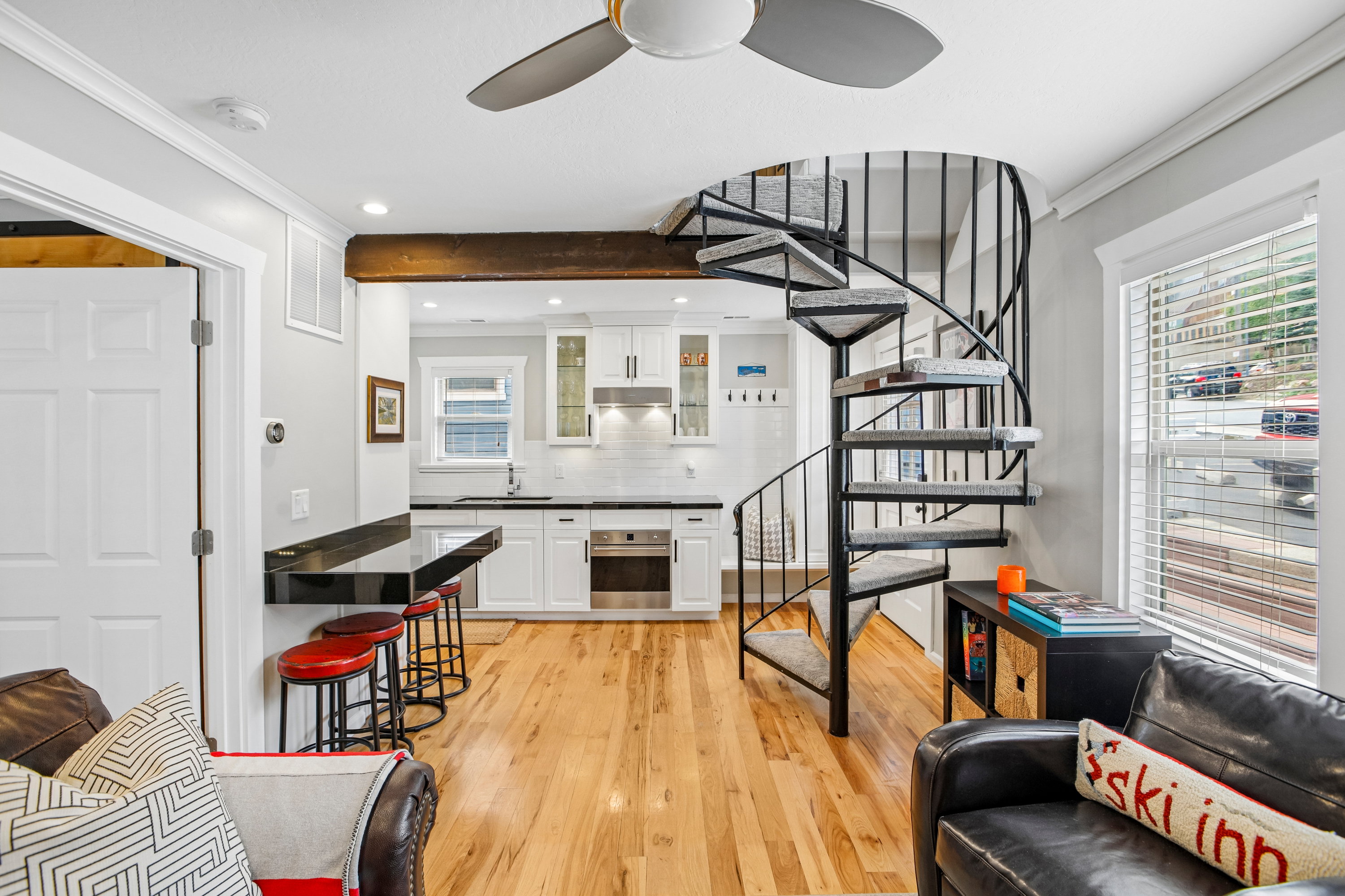 Open-concept living area featuring a spiral staircase, light wood-finish flooring, a contemporary ceiling fan, and a kitchen with white cabinetry and stainless-steel appliances